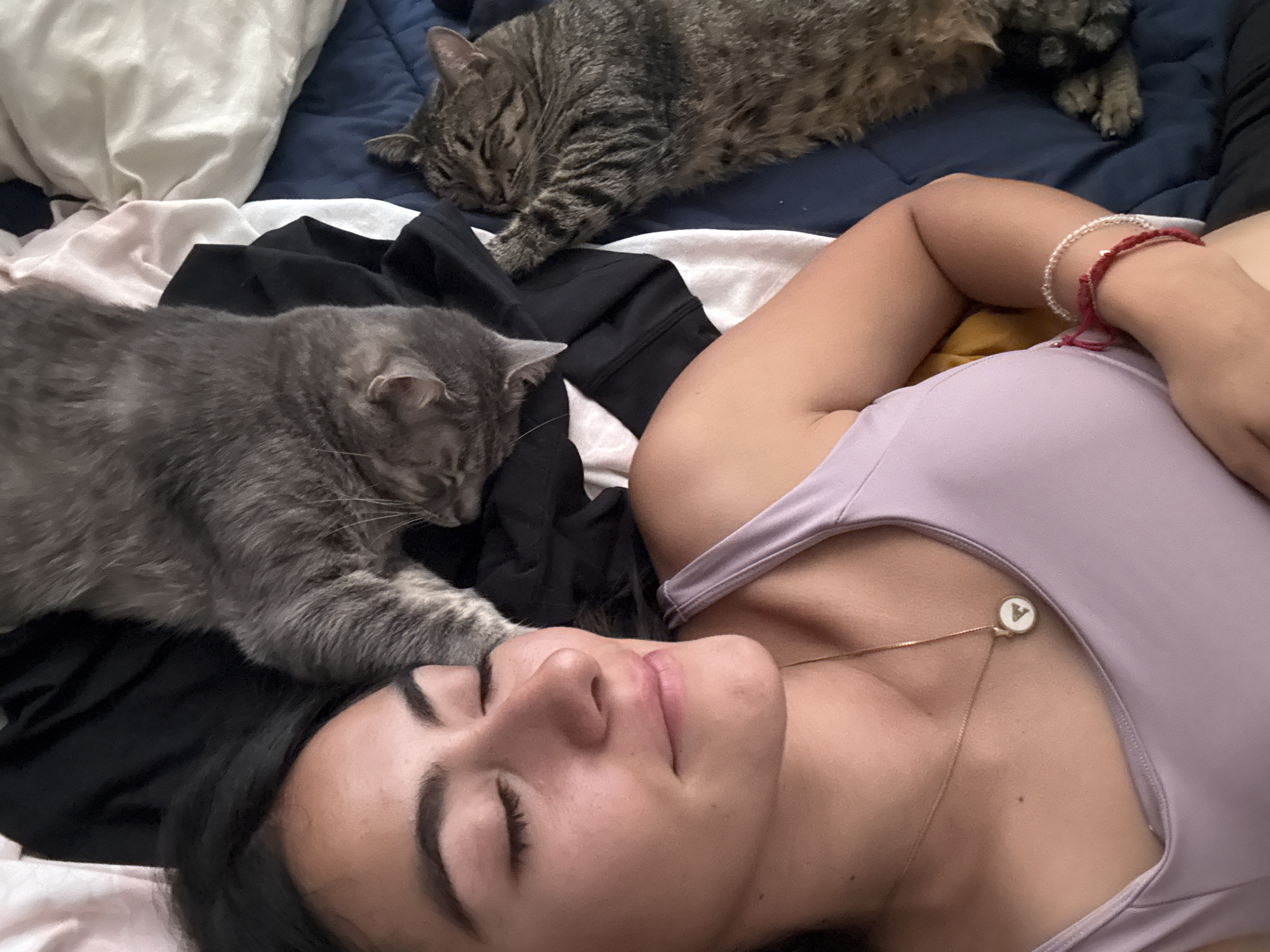 Woman rests peacefully with two cats on bed in Puebla
