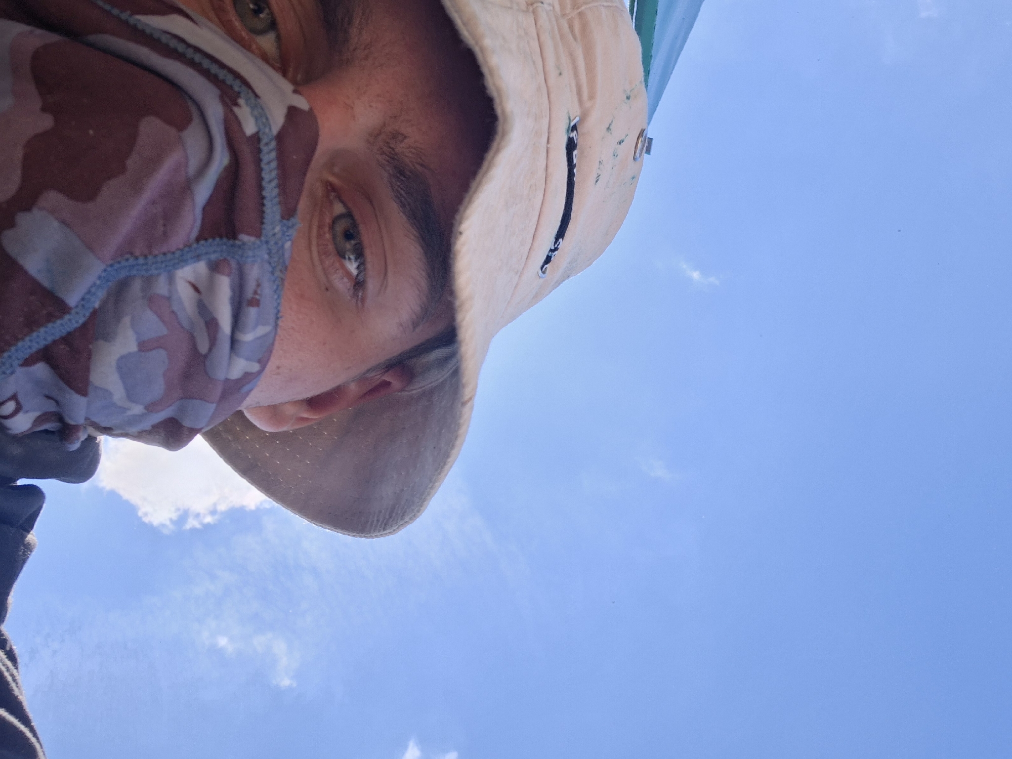 Masked individual photographed against blue sky in selfie