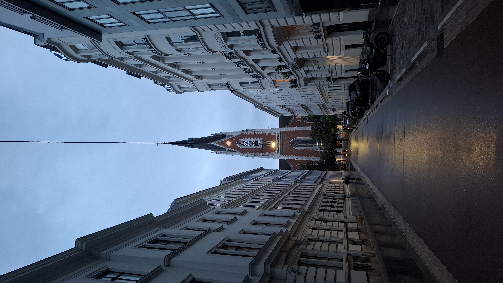 Wet Vienna street with ornate buildings, church spire documented
