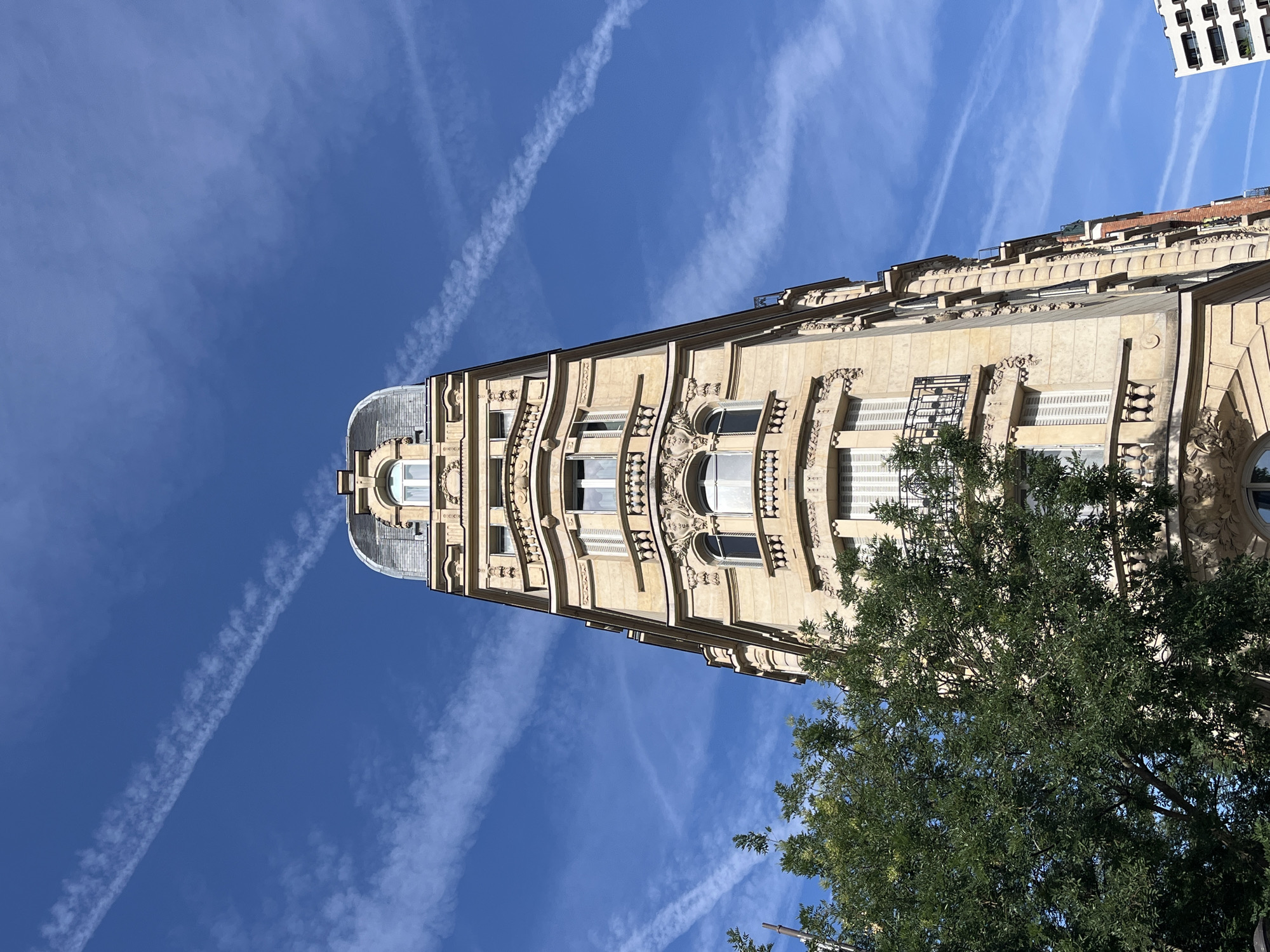 Paris street corner: ornate facades, blue skies, scooter outside a bakery