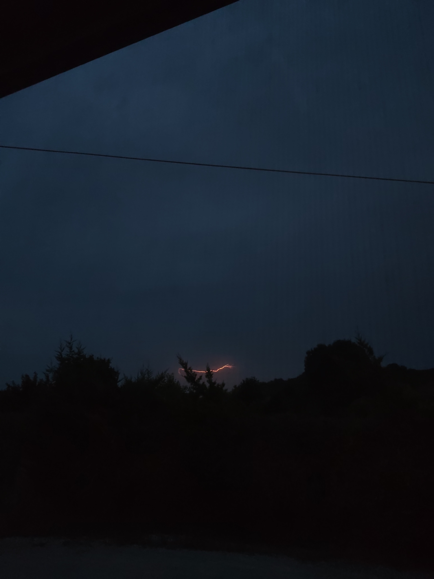 Lightning splits the night sky above a dark treeline.