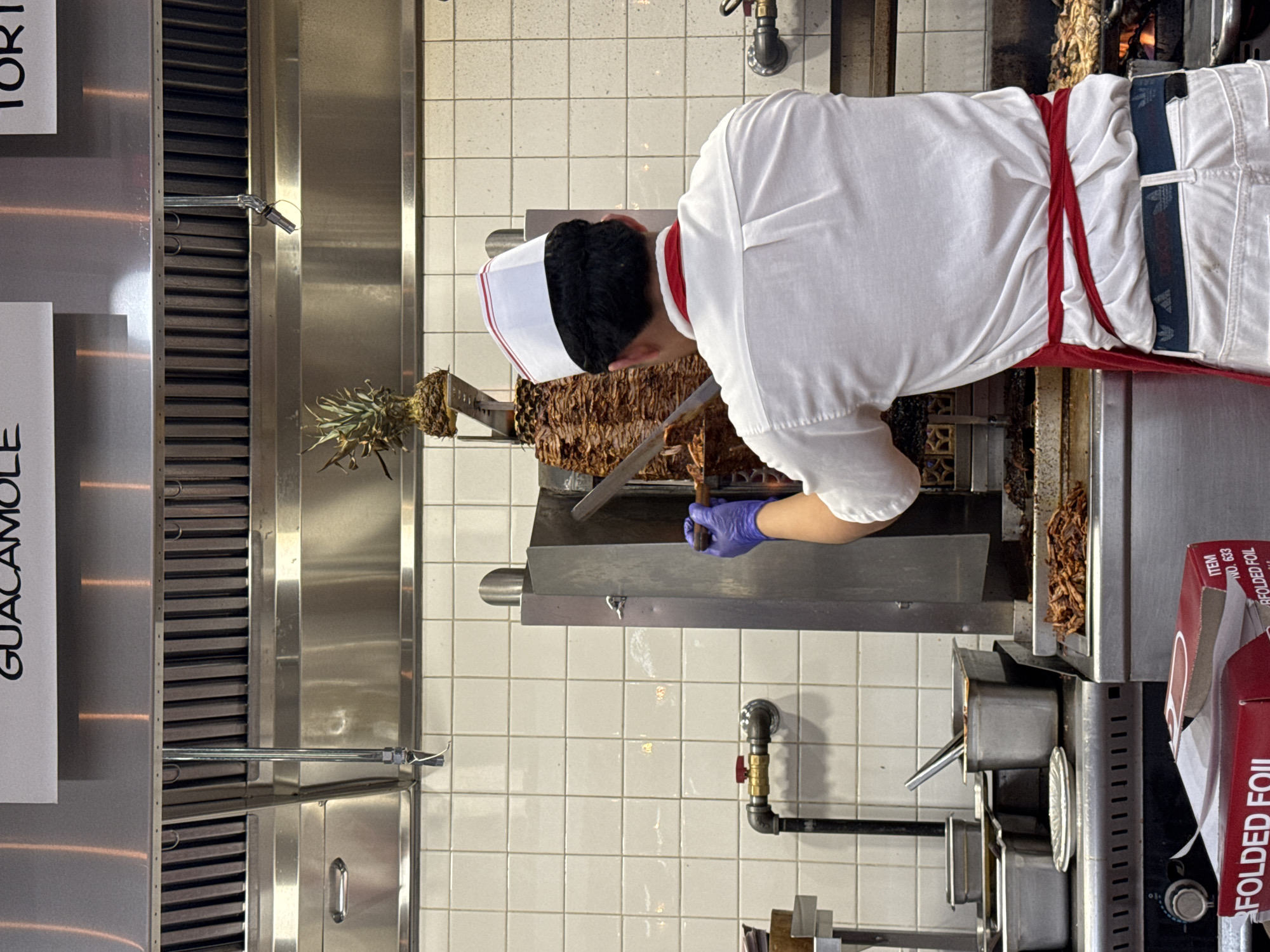 Kitchen worker slices meat from vertical spit in NYC