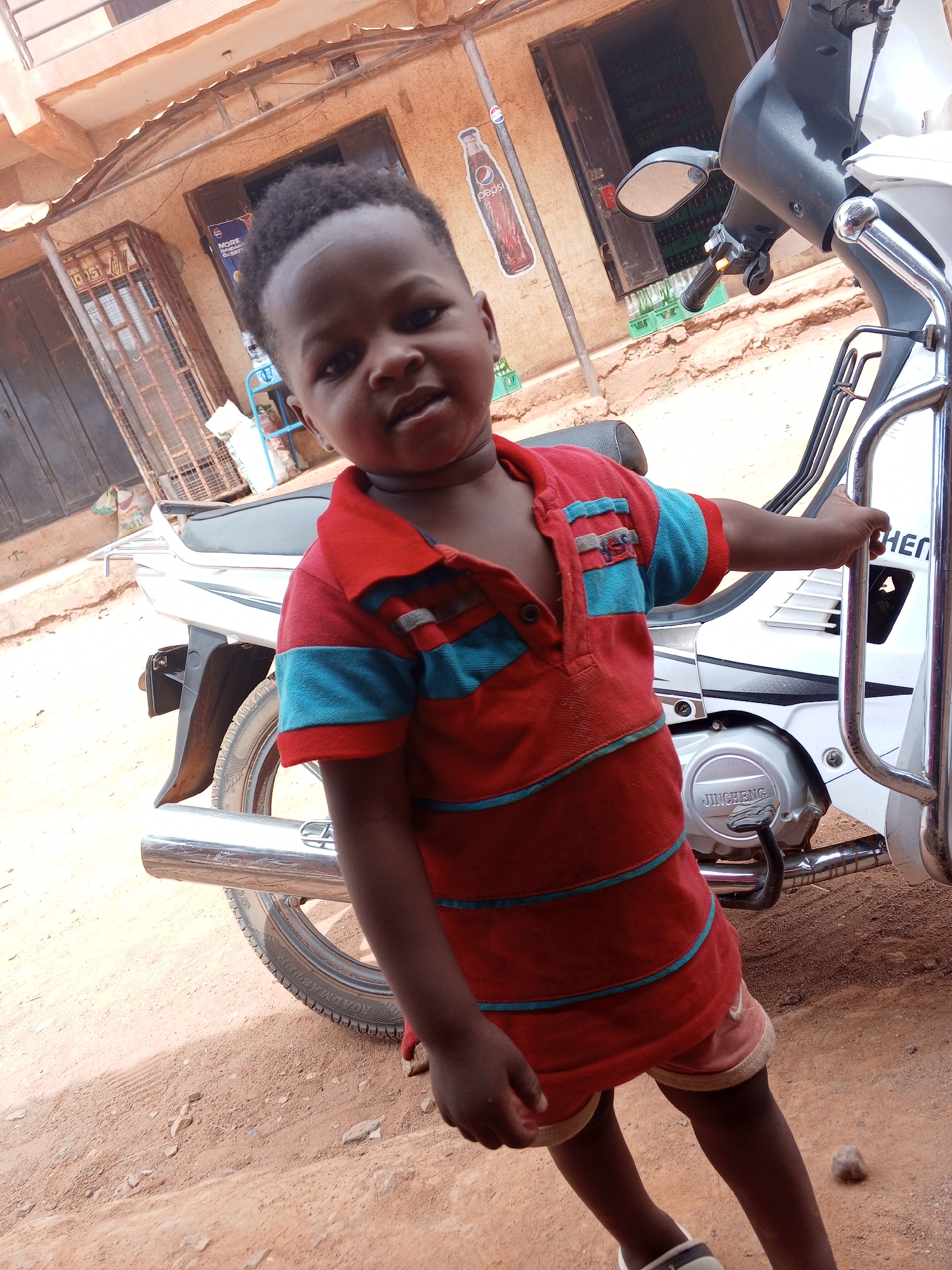 Child poses with white motorcycle in Yelwa, Nigeria