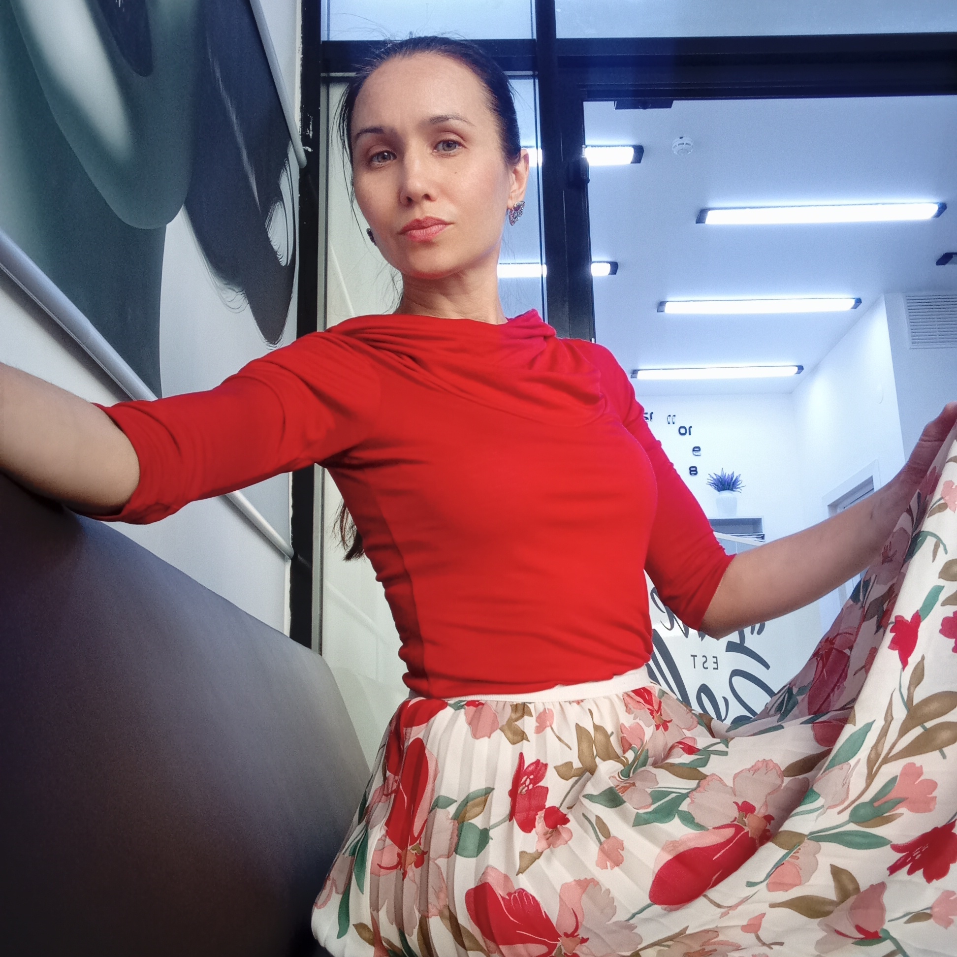 Woman in red top, floral skirt poses indoors in Izhevsk