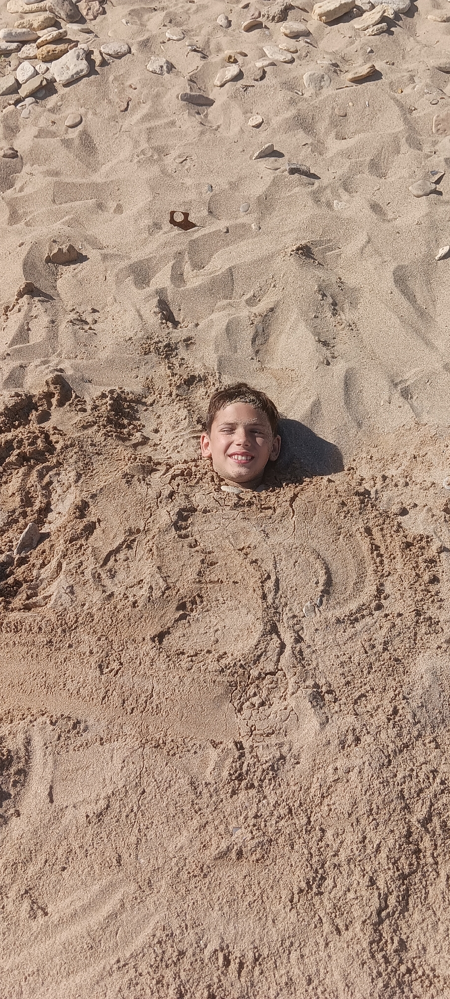 Head buried in beach sand, all smiles