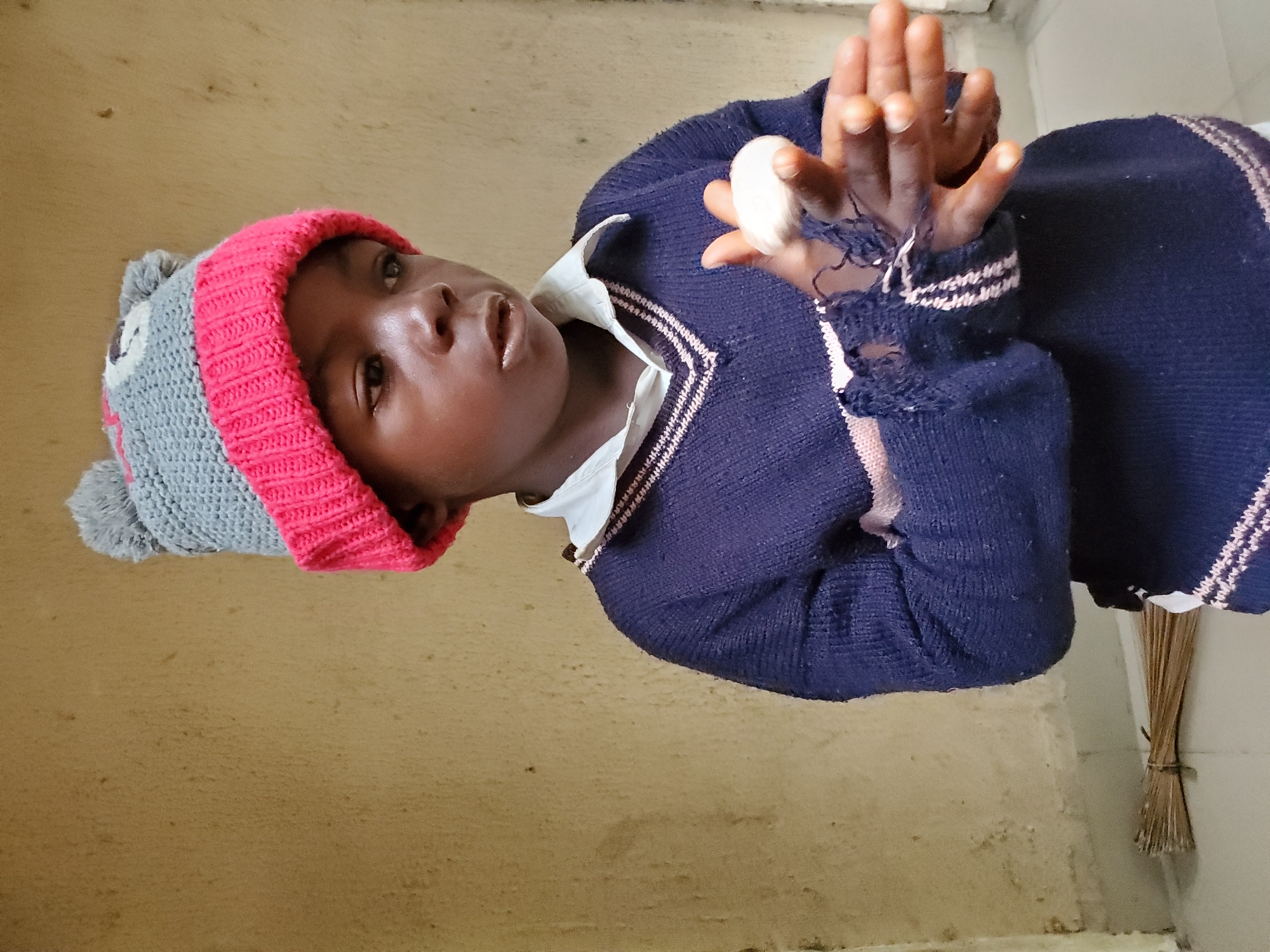 Child examines object indoors while ducks gather outside Mararaba building