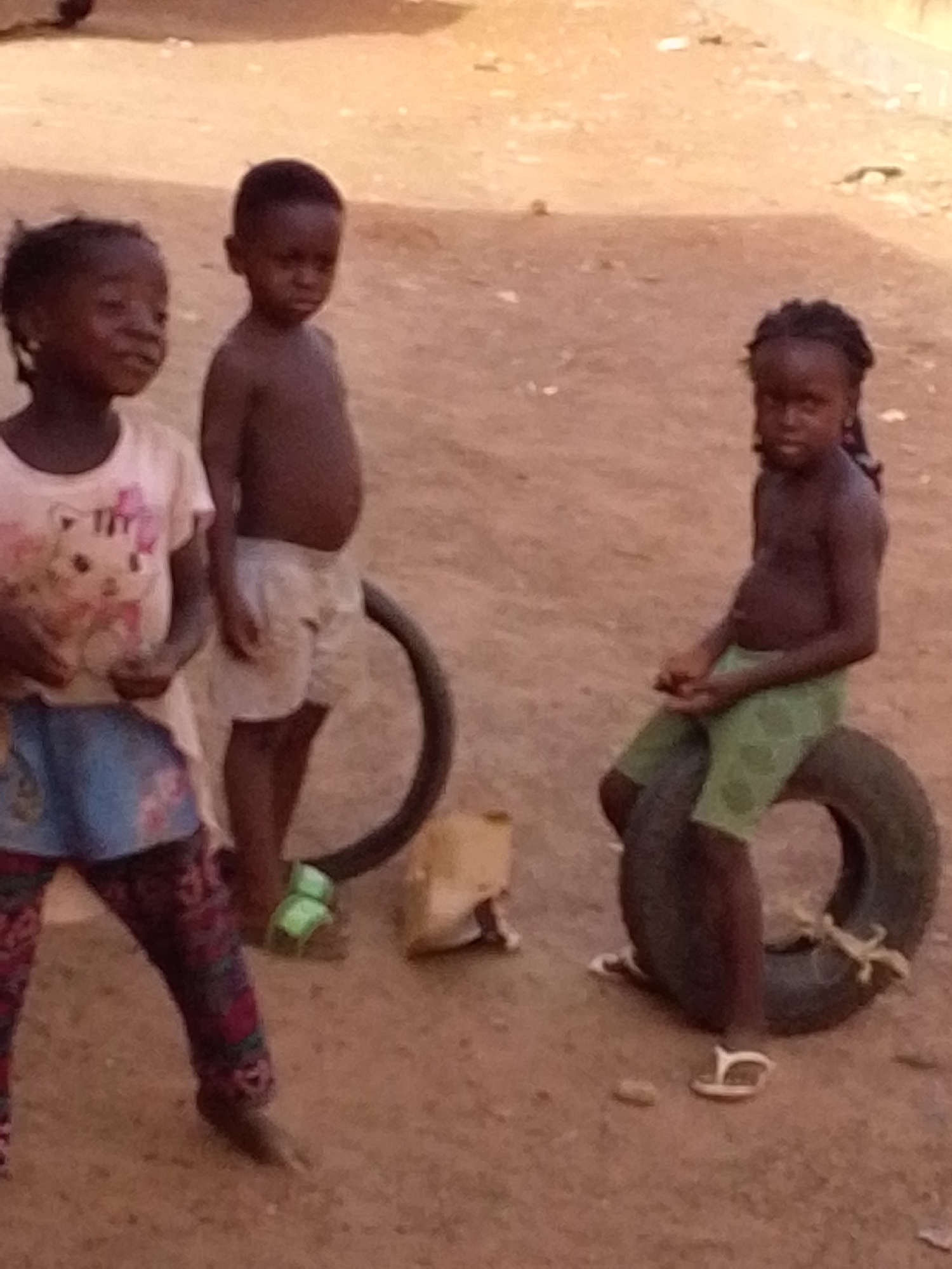 Three children gather, one sitting on tire