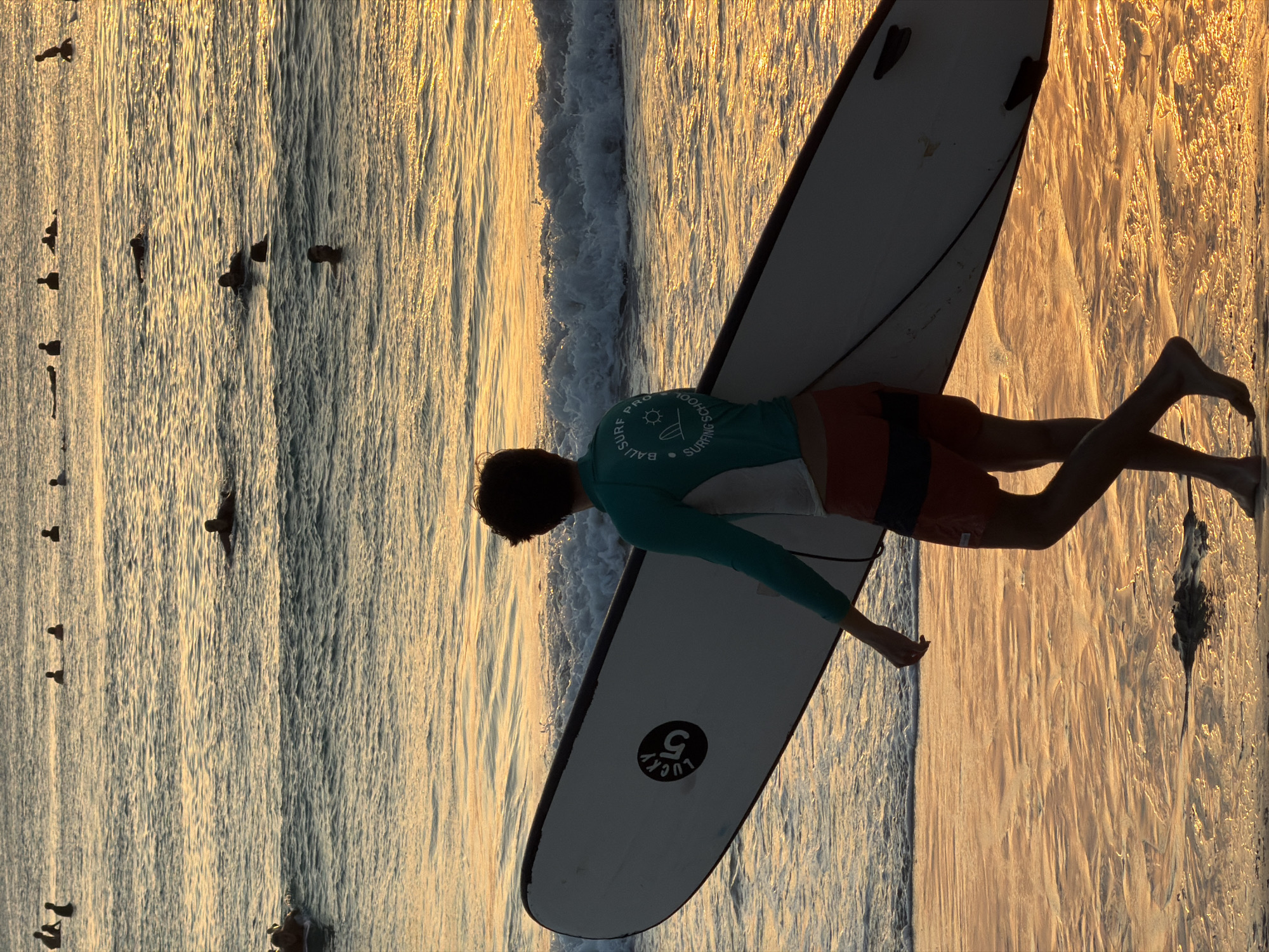 Sunset crowd at Kuta Selatan — surfers, sand, and a dog