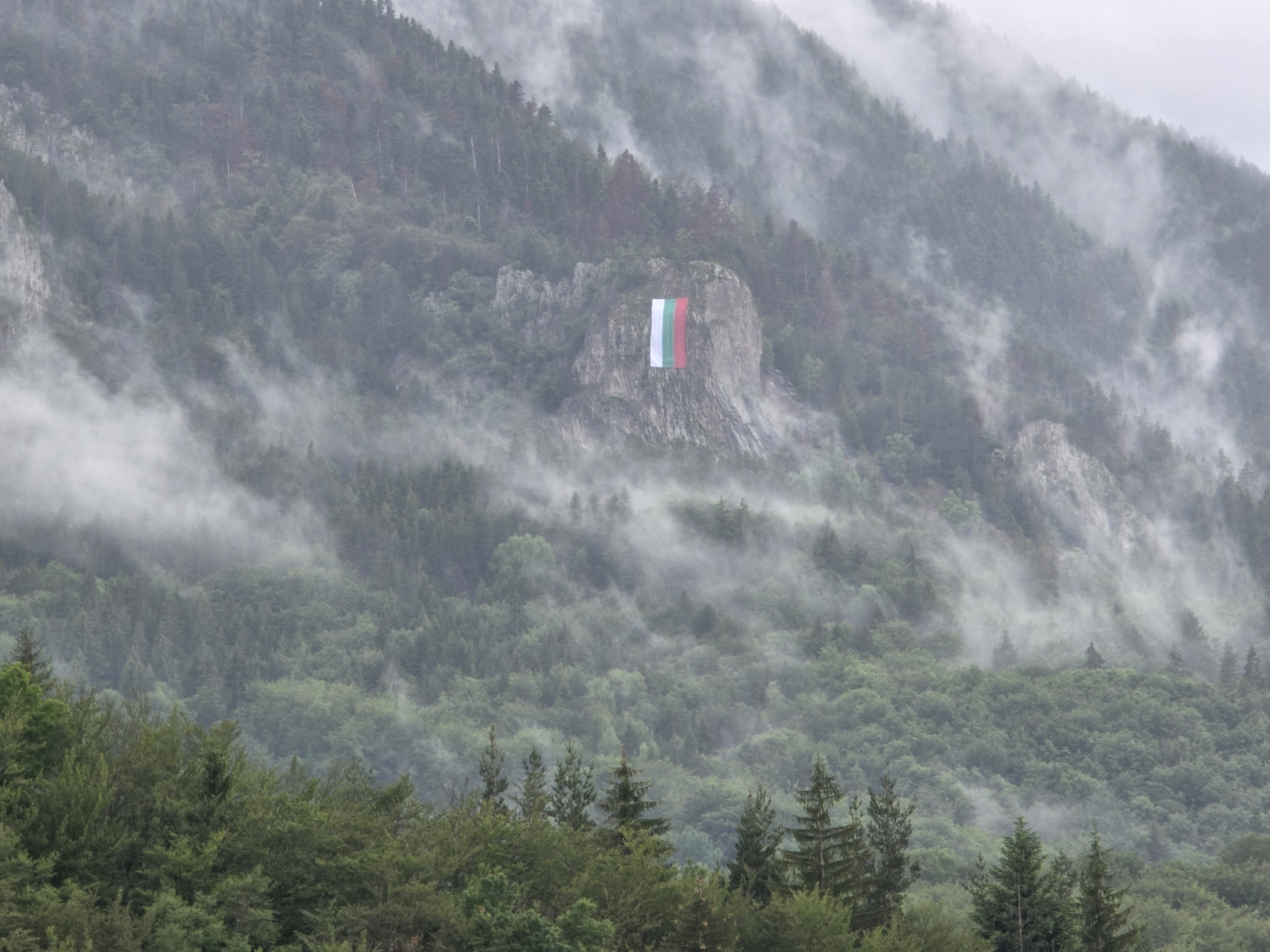 Bulgarian flag displayed on misty mountain outcrop near Smolyan