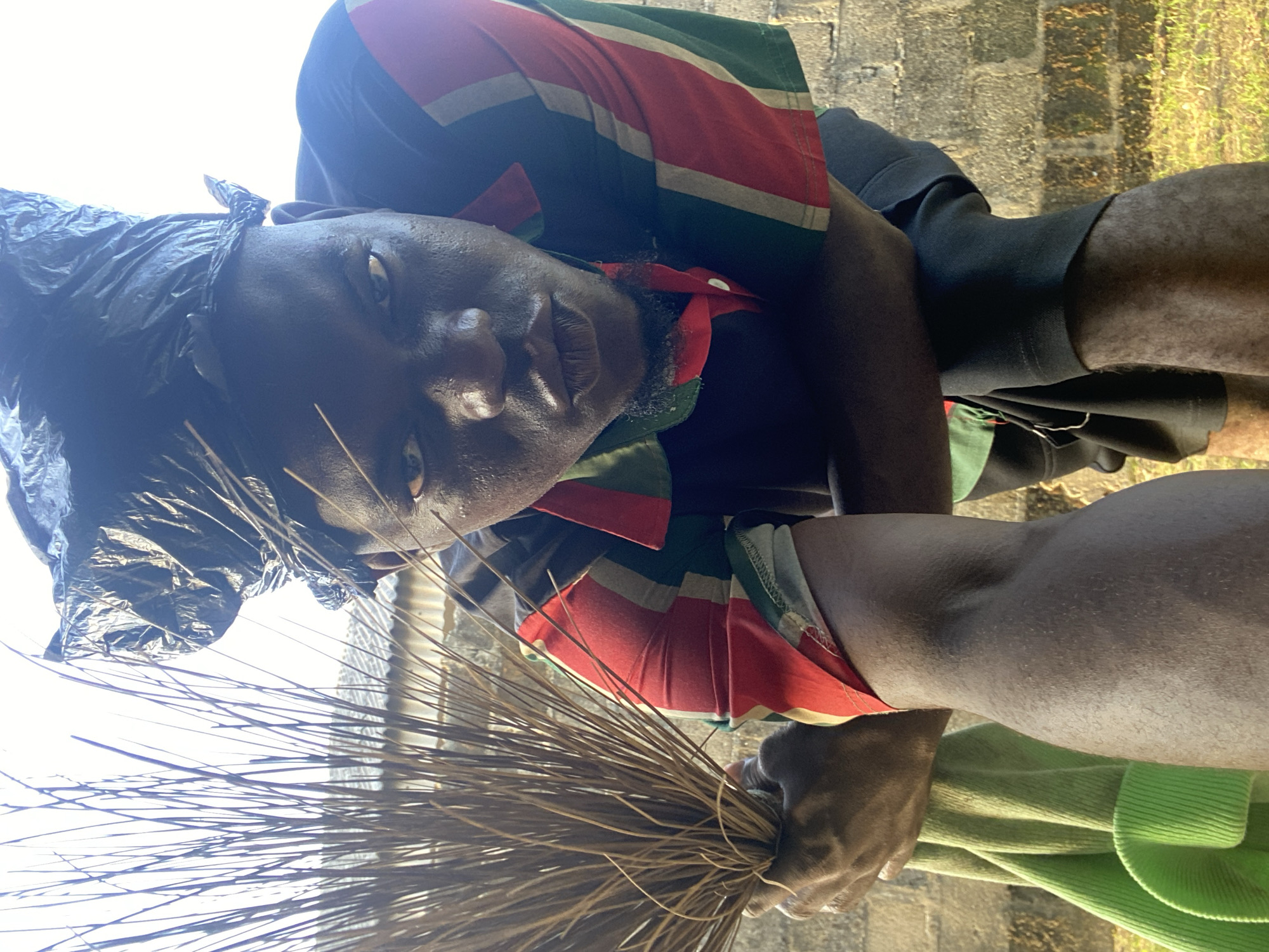 Two people photographed outdoors in colorful clothing, one holding broom