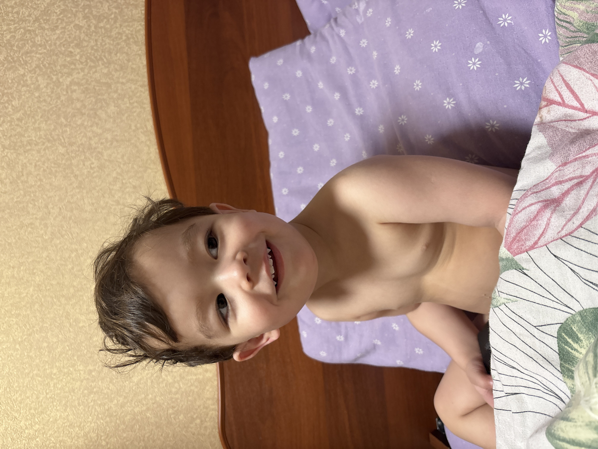 Child smiles while lying on floral bedsheets in Chaikovsky