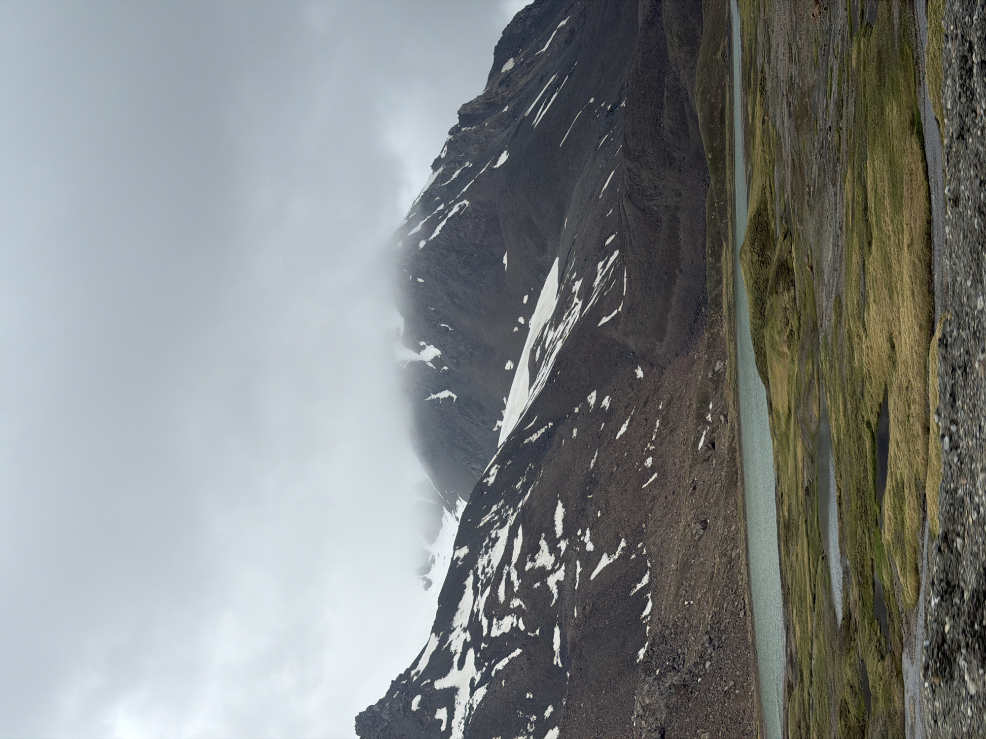 Remote Kyrgyz highland terrain, rocky slopes and snowfields under cloud