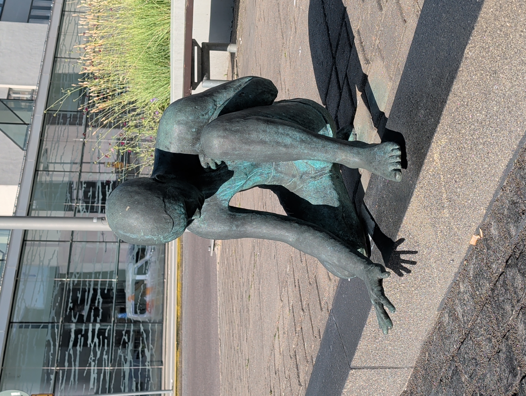 Contemplative bronze sculpture seated on a concrete curb, Stockholm