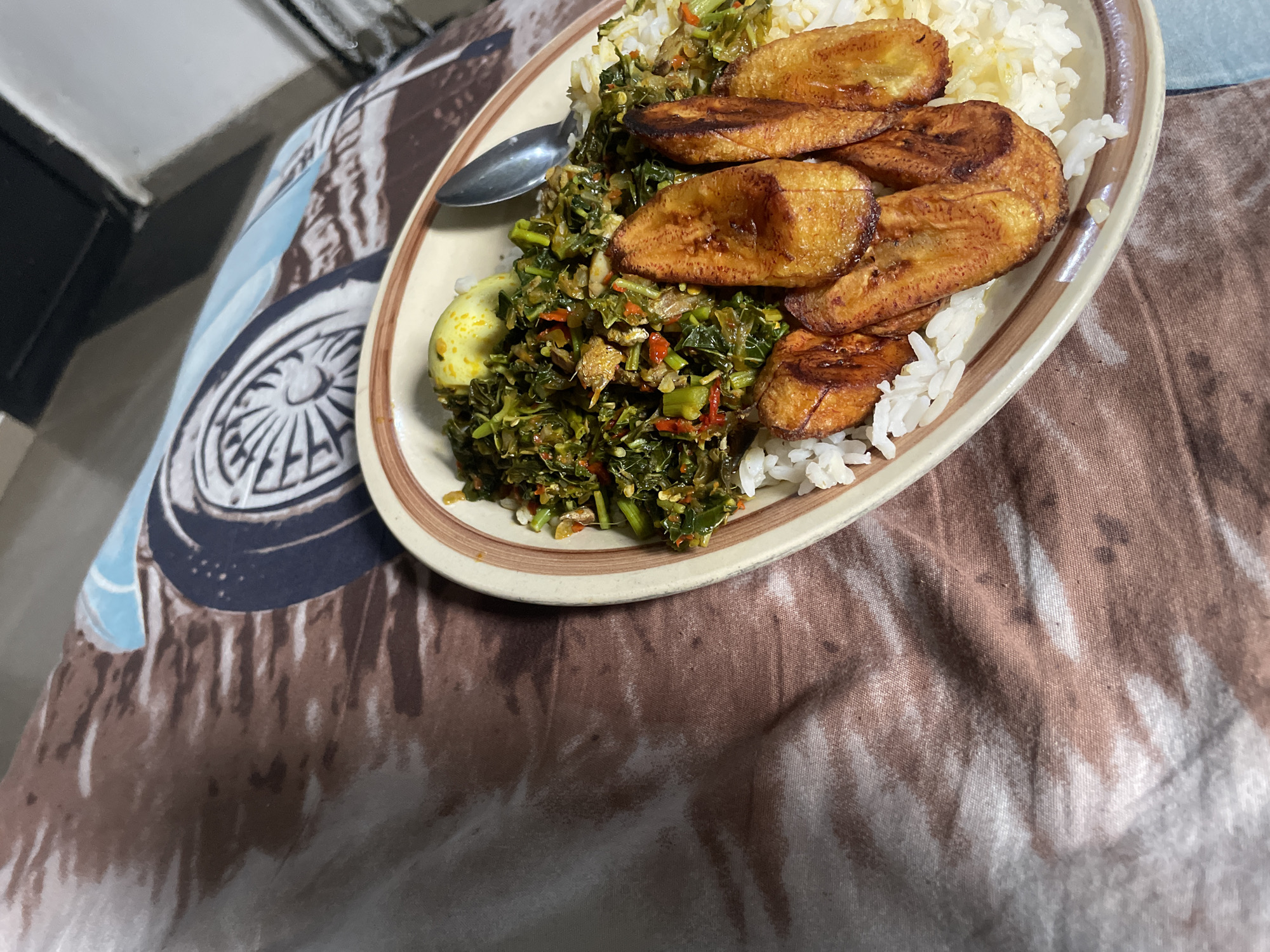 Nigerian plate of rice, plantains, and greens on patterned fabric
