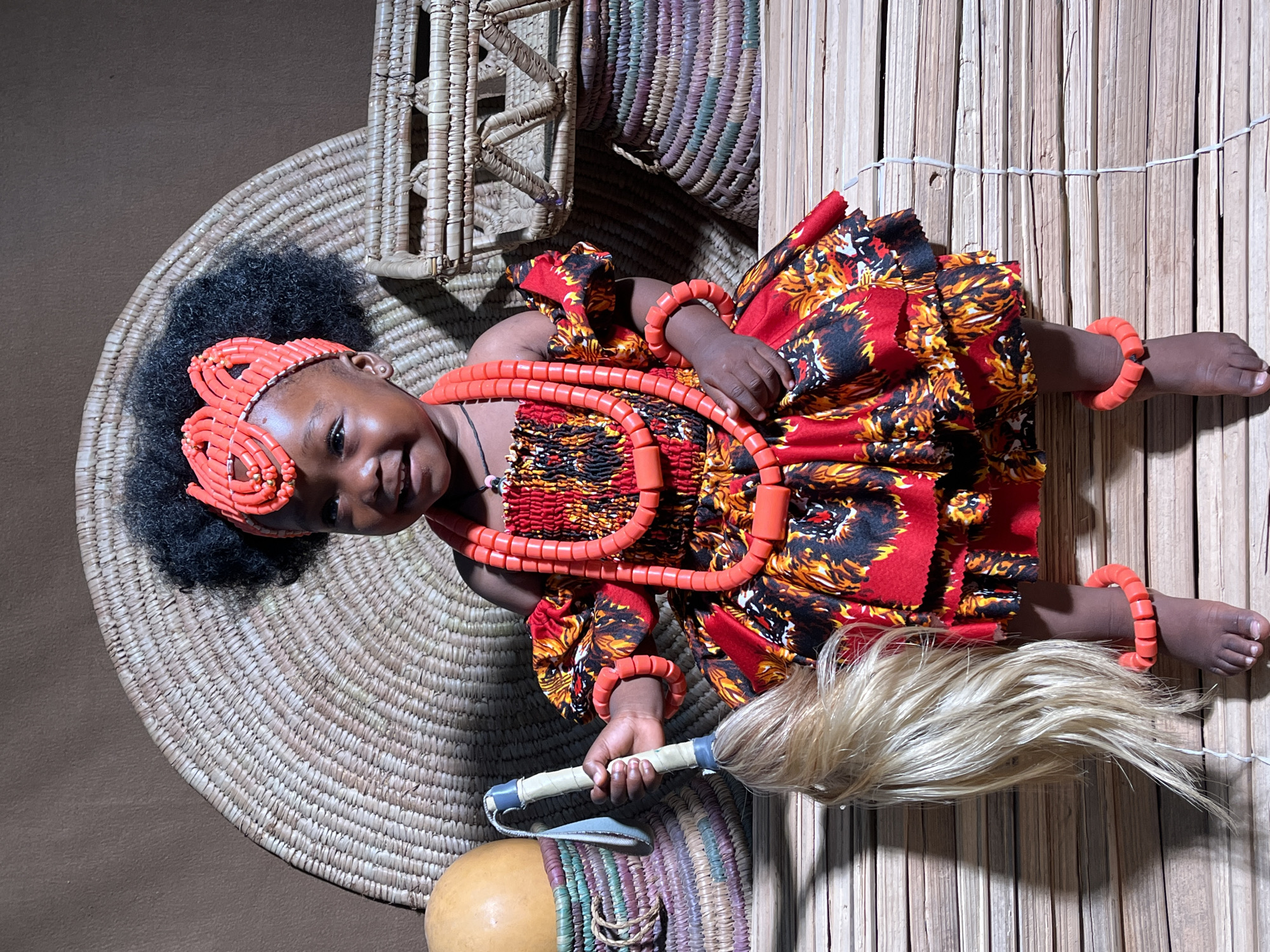 Child in traditional Nigerian ceremonial dress documented on woven mats