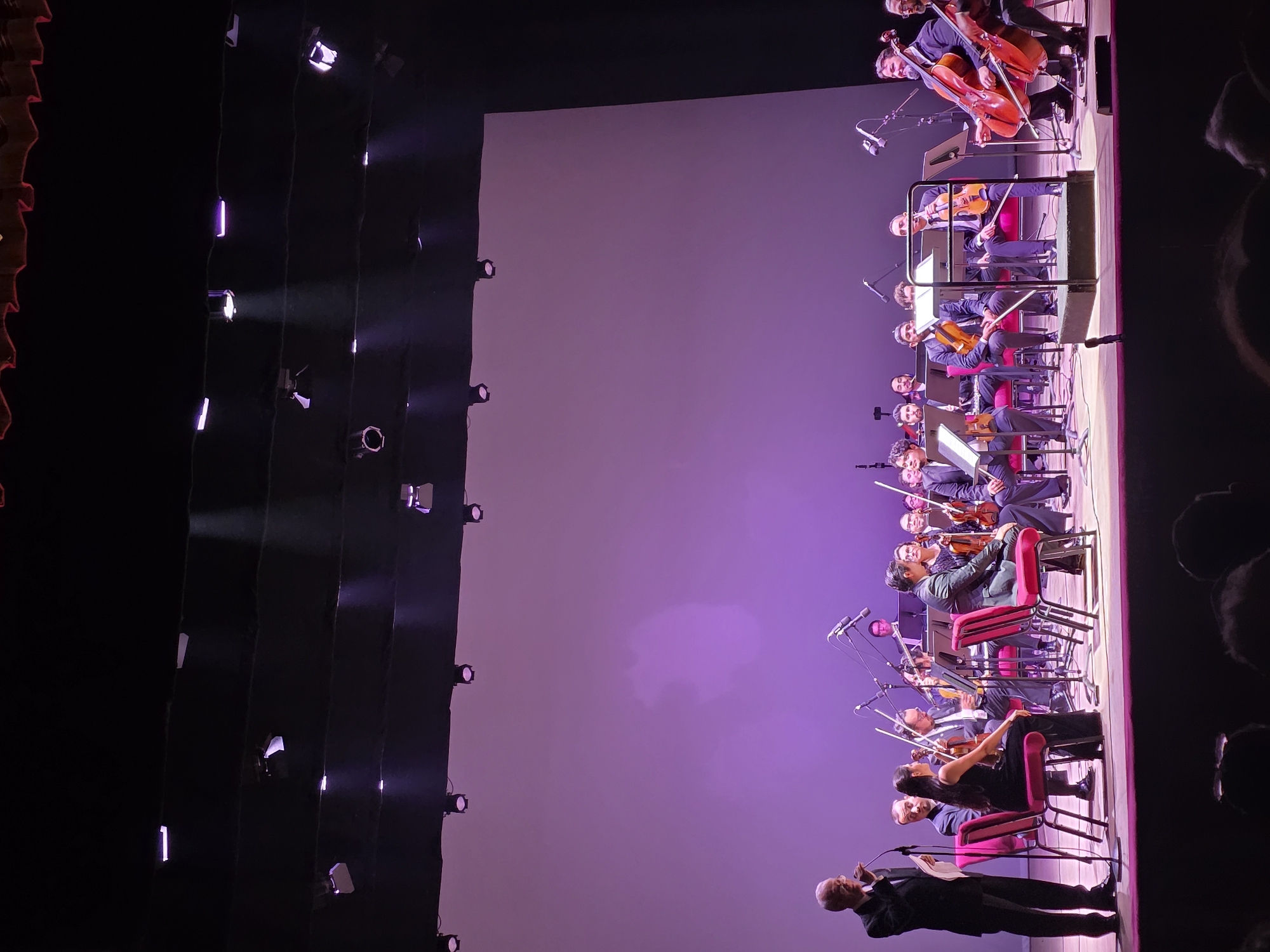Orchestral performance underway on a purple-lit stage in Iquique