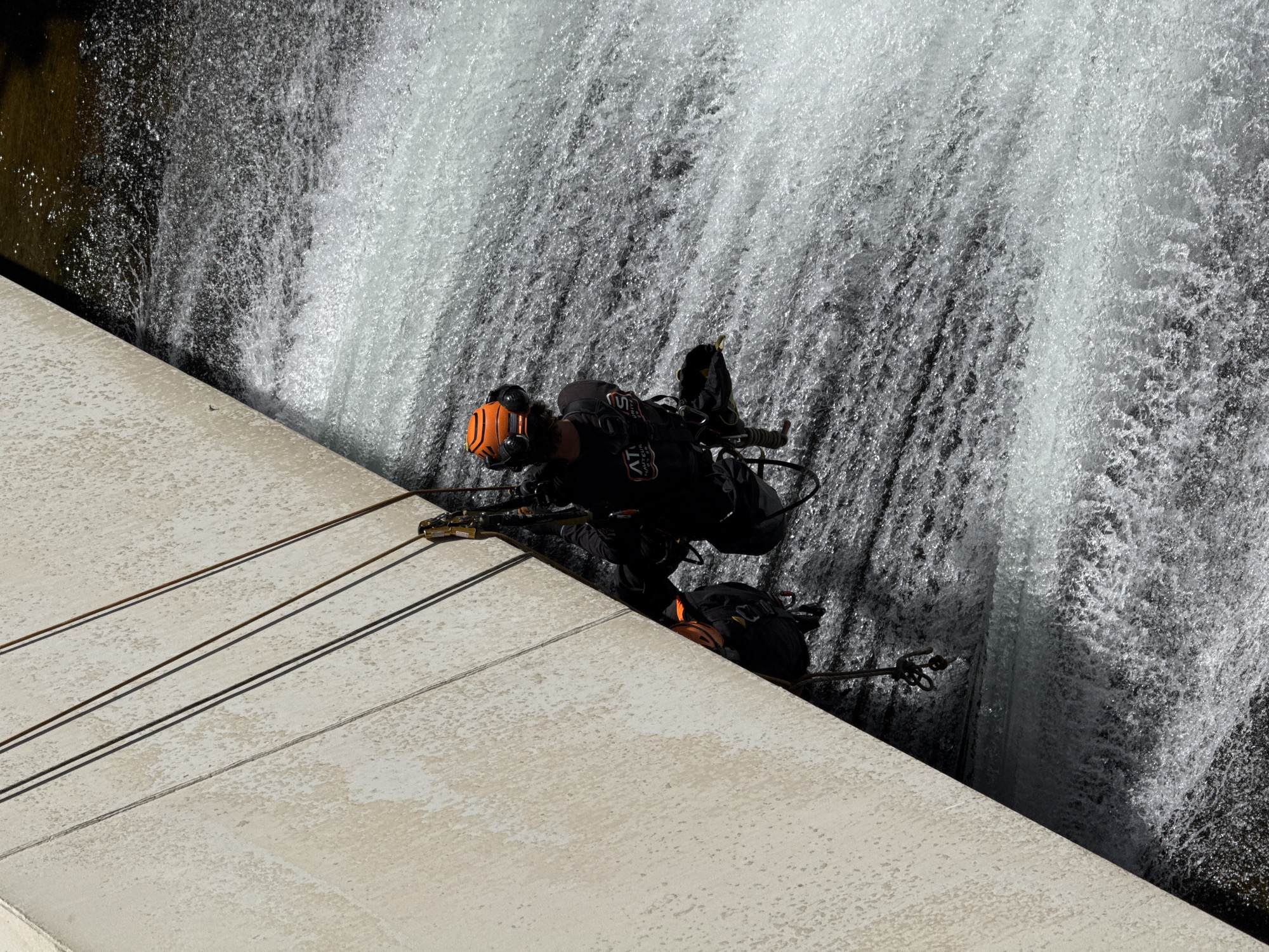 Two rappellers descend concrete dam face in Curbans, France