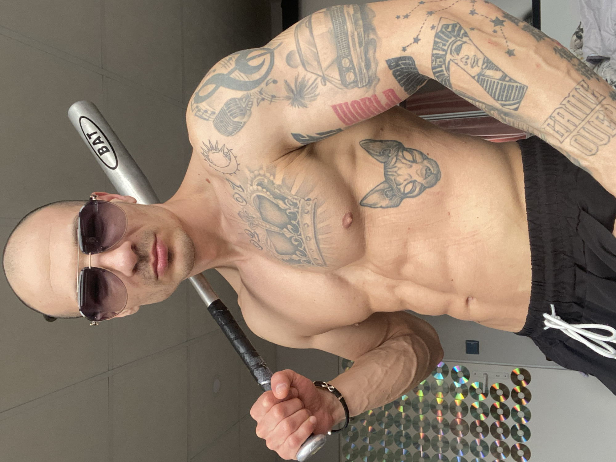 Man poses with baseball bat in CD-decorated room