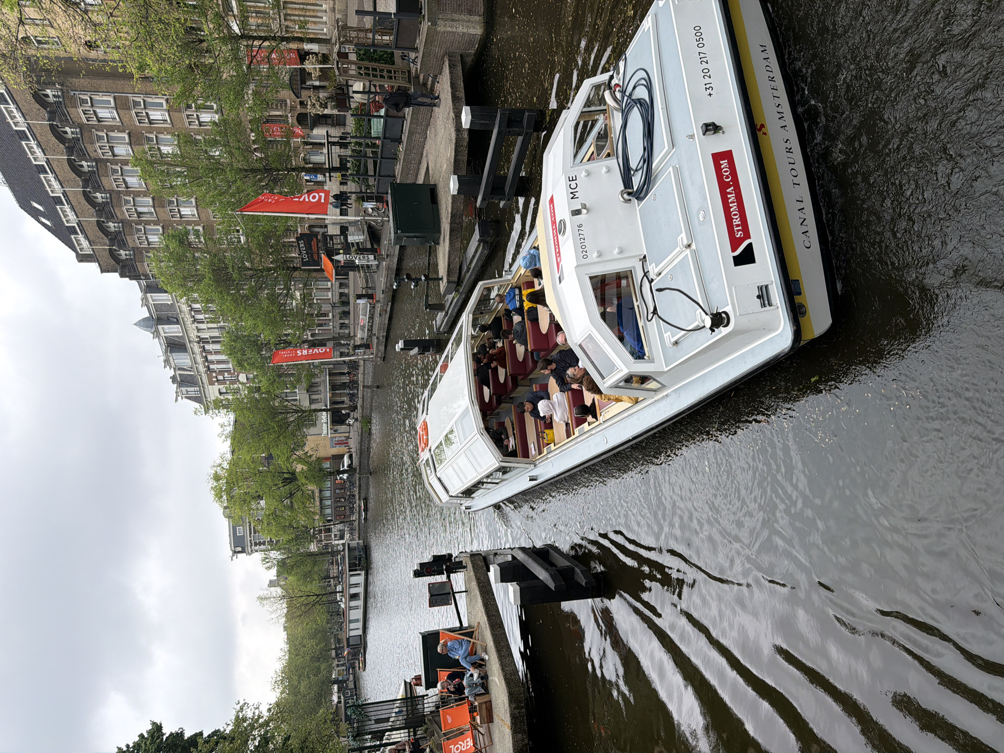 Tourist boat navigates Amsterdam canals past waterfront dining area
