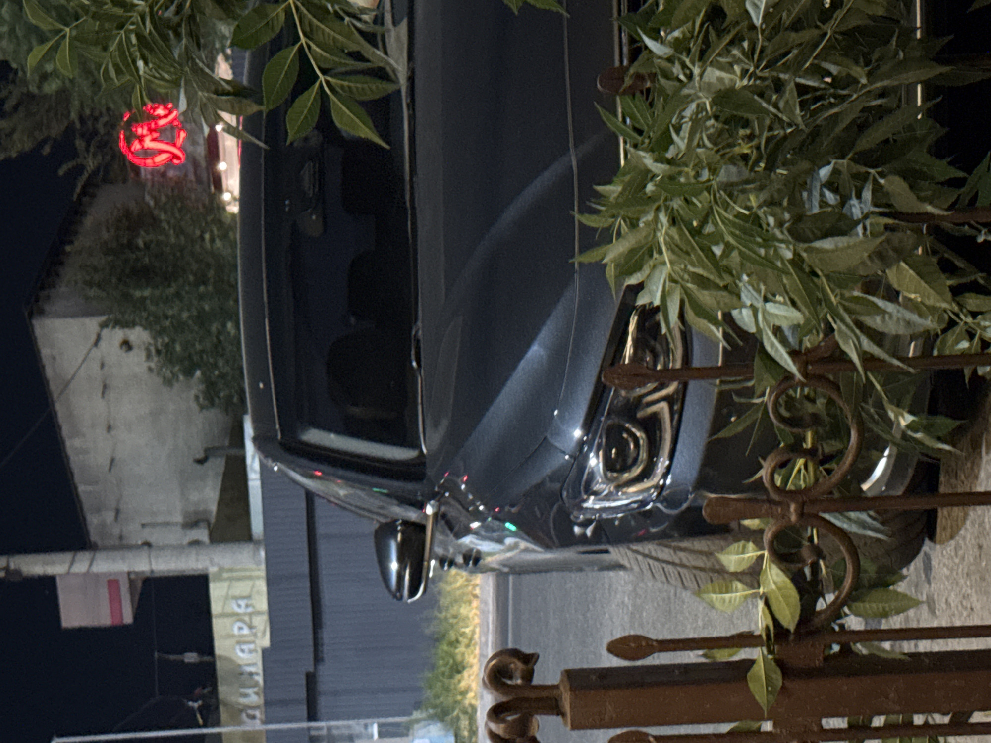 Dark sedan parked at night near Shymkent intersection, headlights on