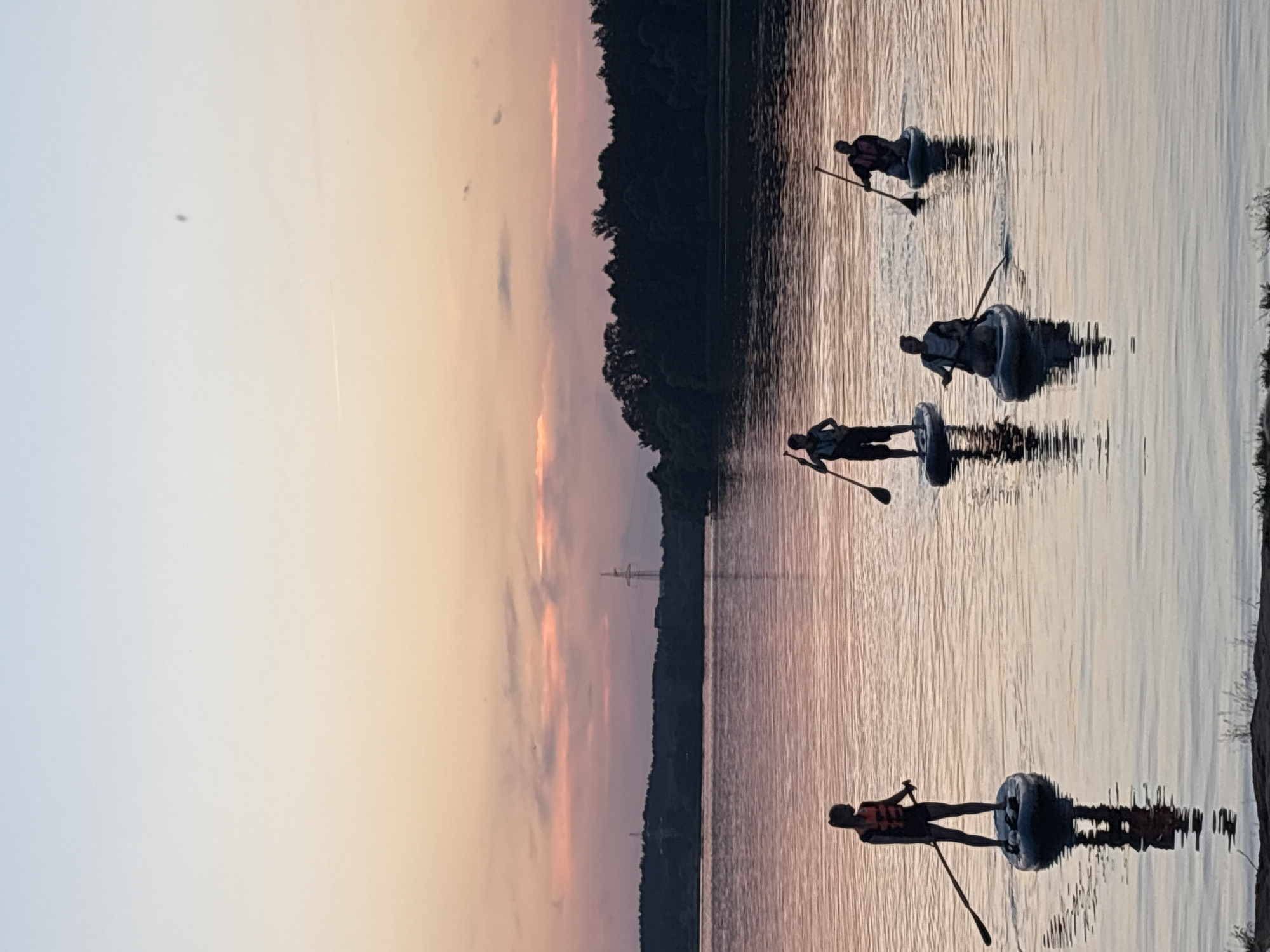Golden-hour lake scene with paddleboards, pedal boats, and a slow sunset