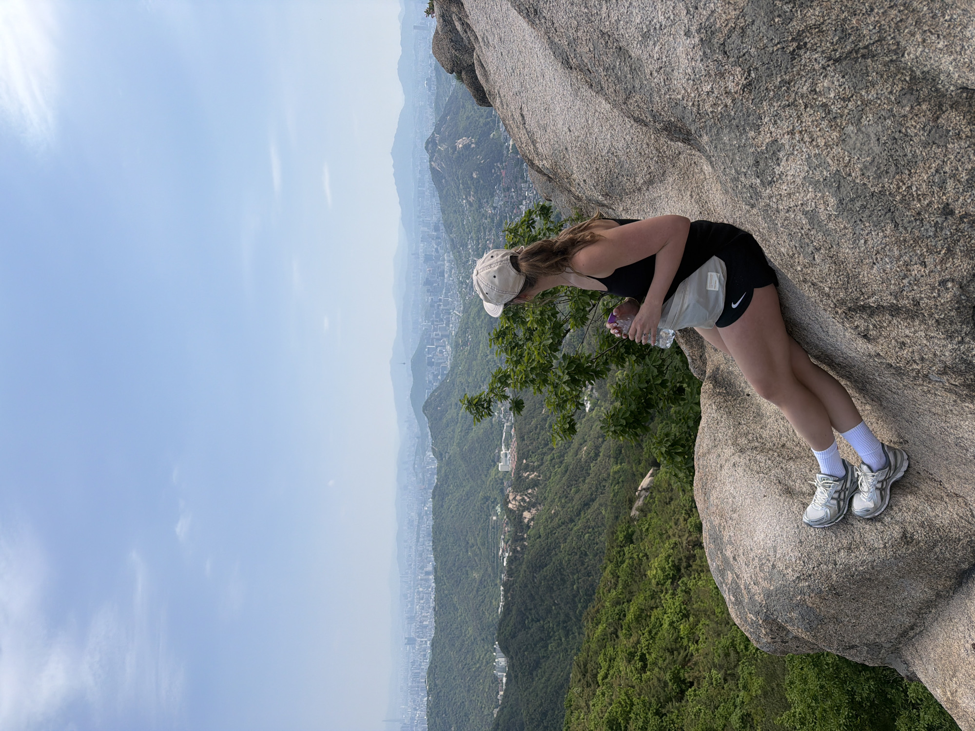 Early morning hiker surveys Seoul cityscape from mountain boulder