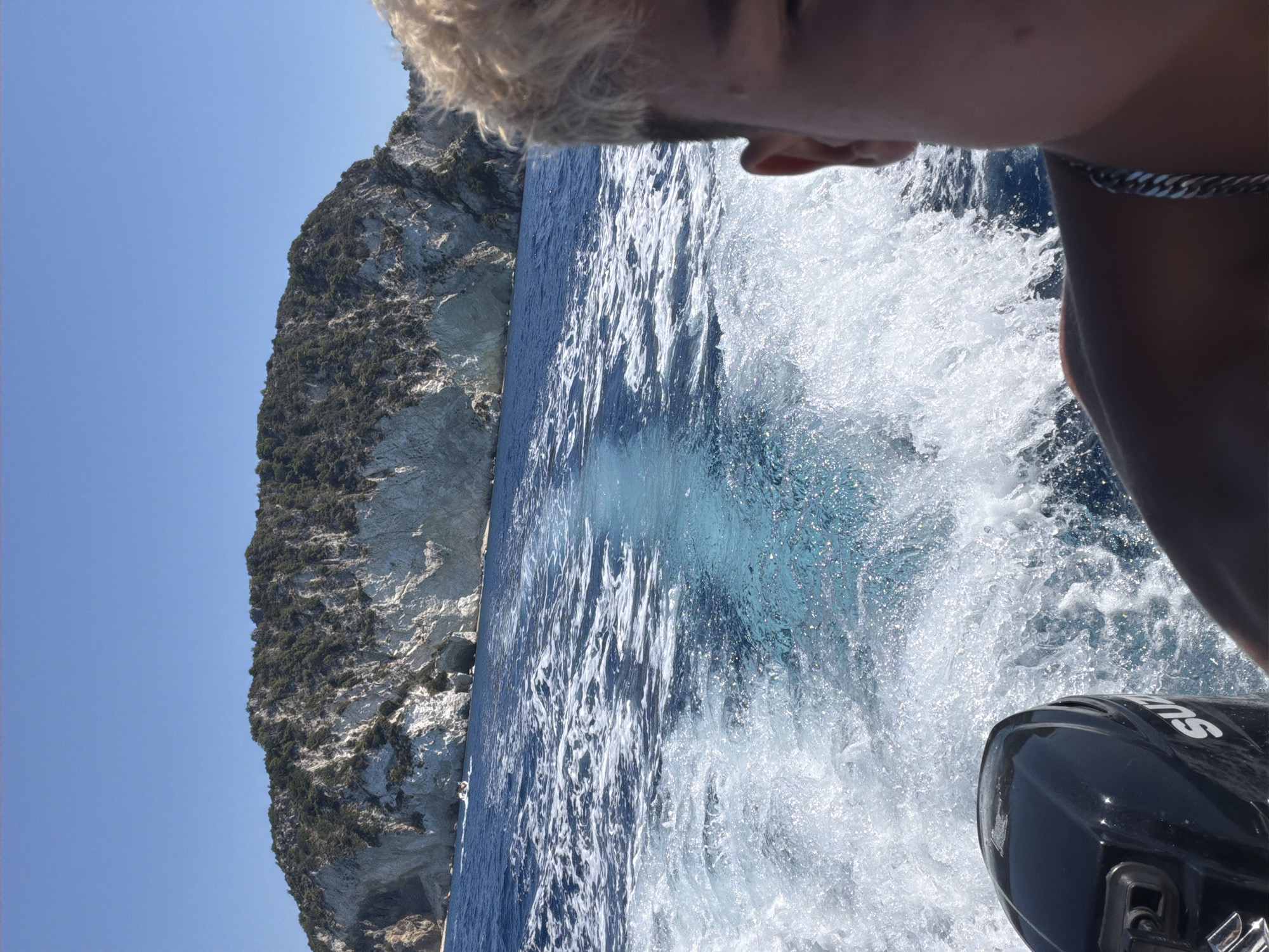 Boat cruising past a rocky island in open blue water