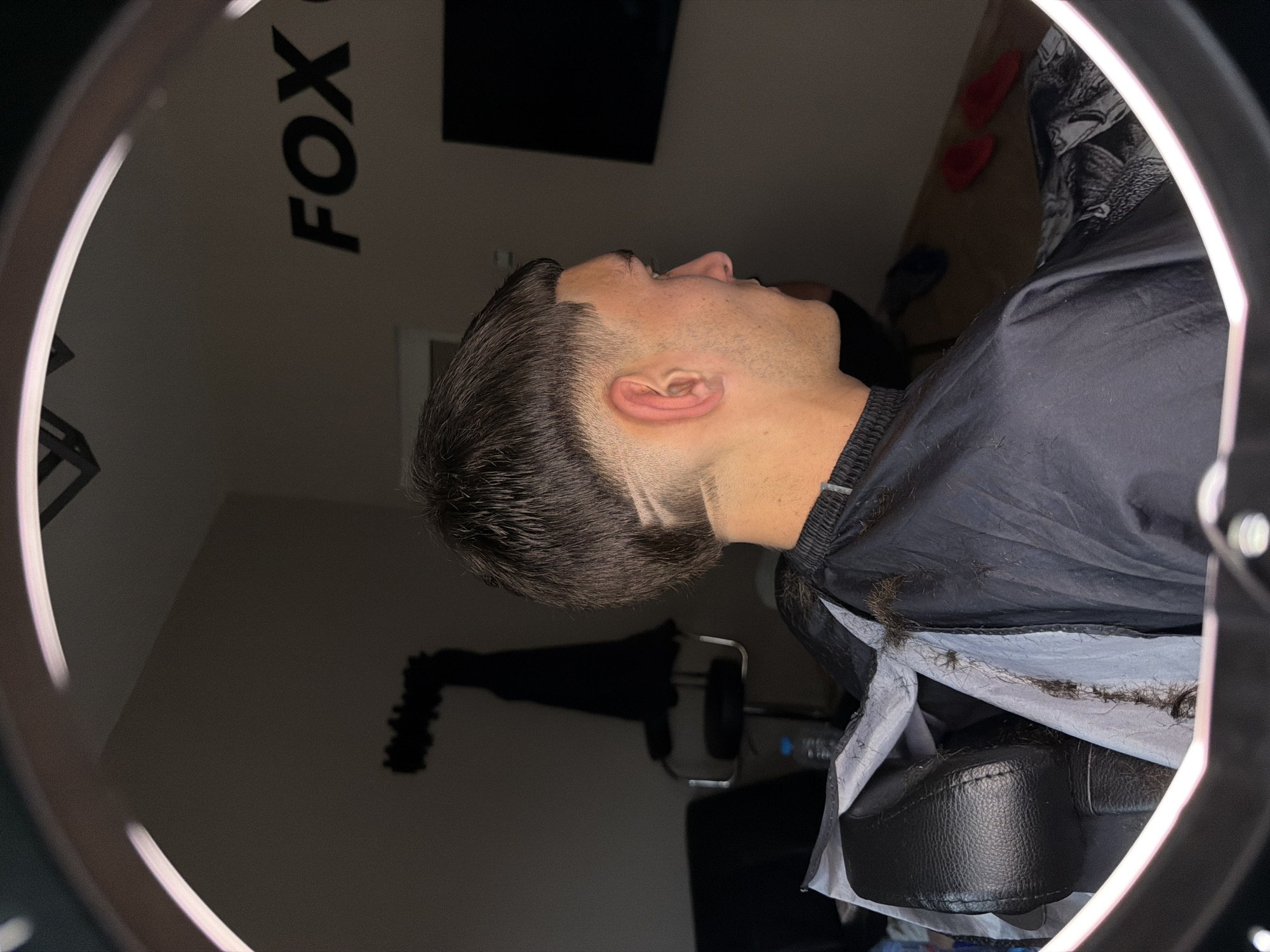 Man gets haircut at Septemvri barbershop under ring lights