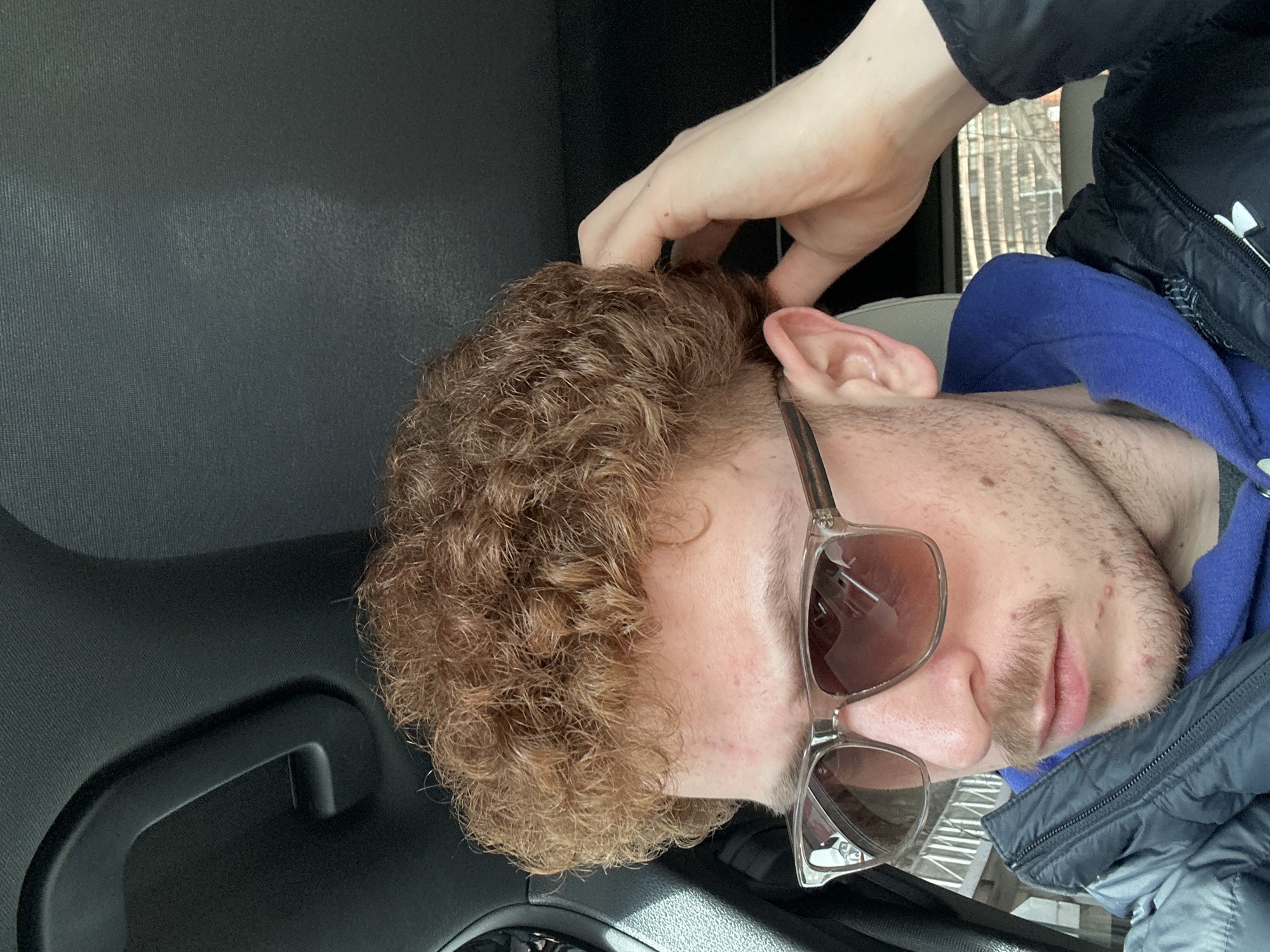 Man in sunglasses sits in car touching hair