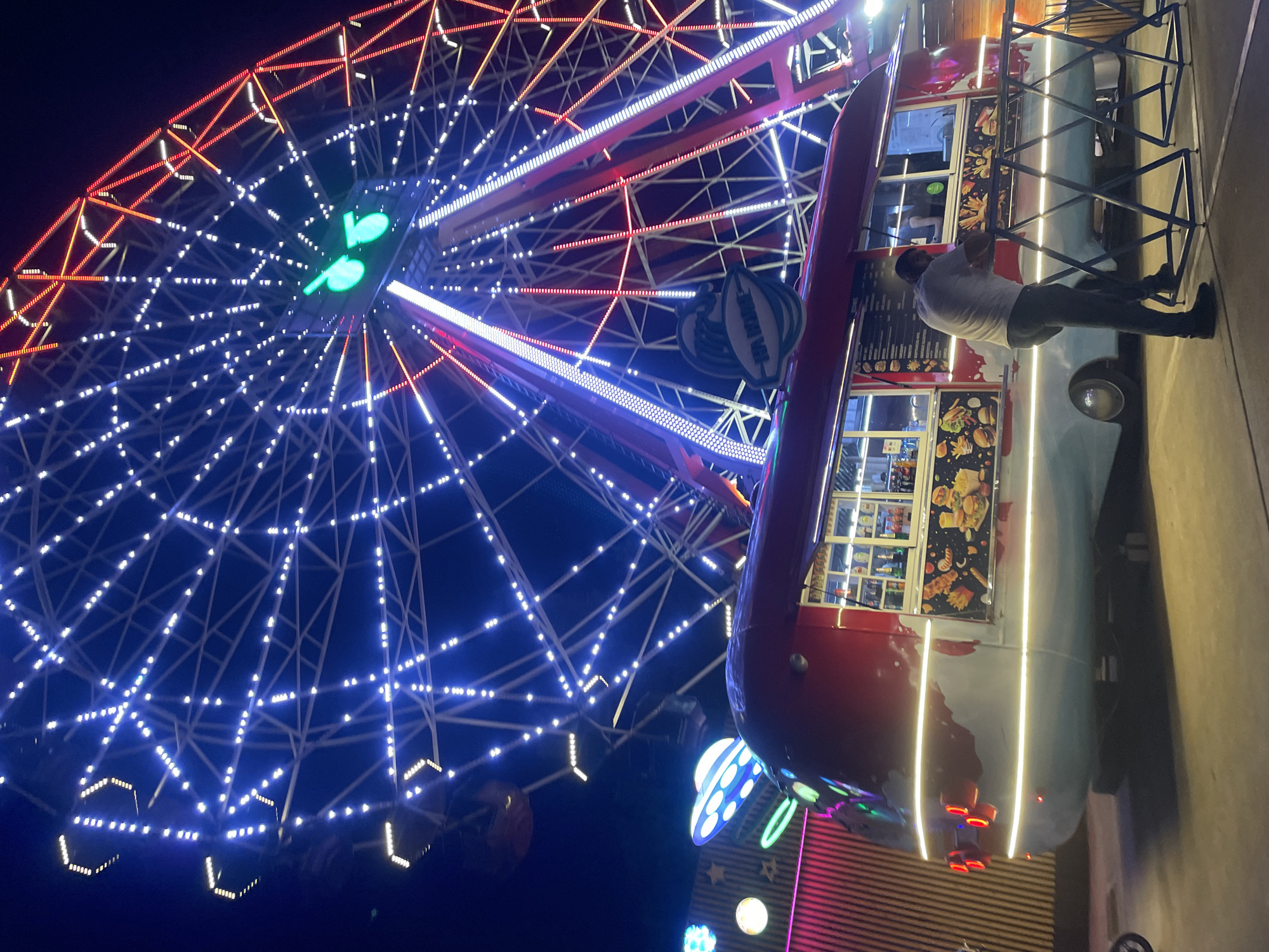 Illuminated Ferris wheel and food truck at a night fair in Sadovyi