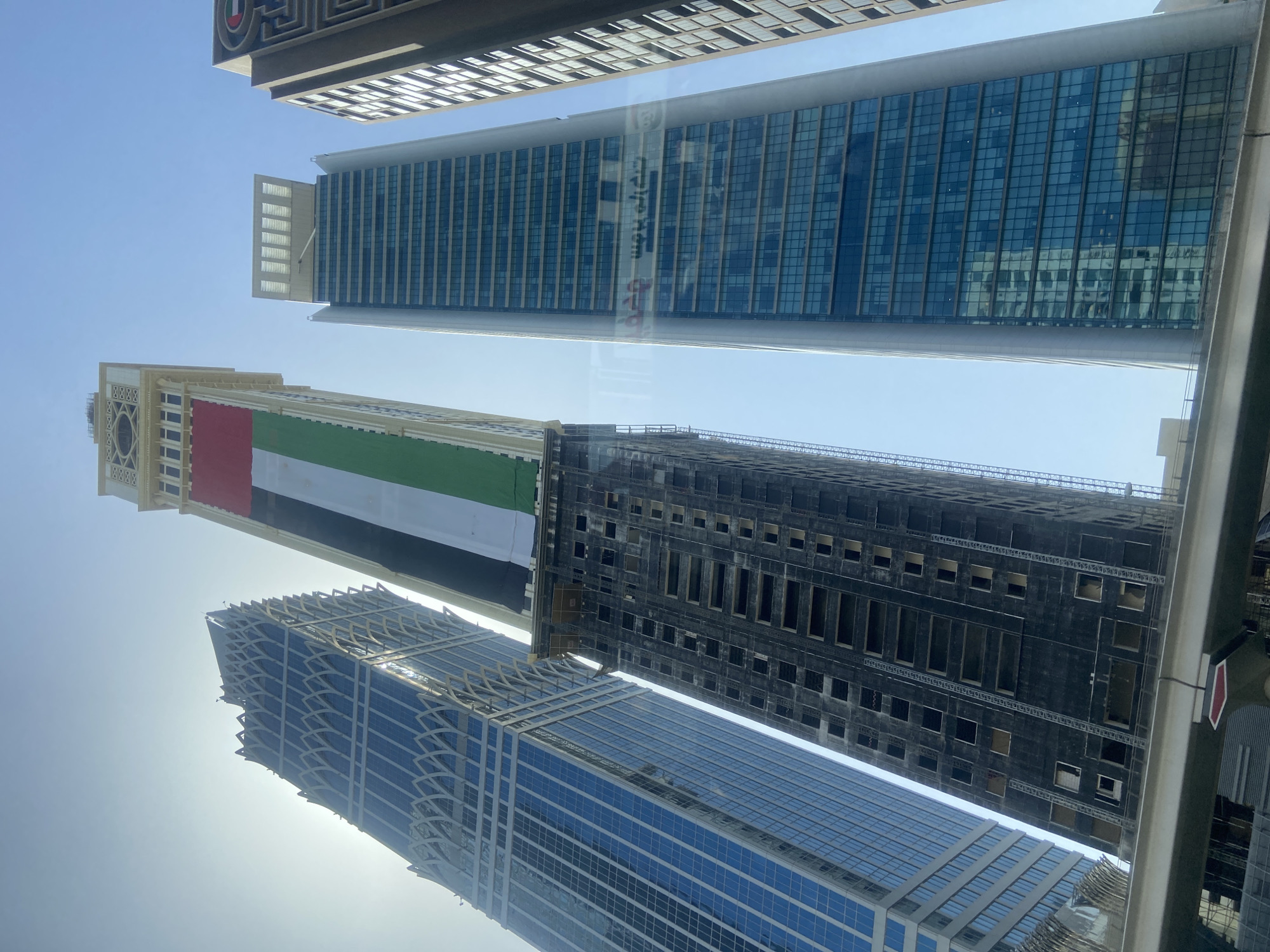 Dubai skyscrapers display UAE flag against clear morning sky