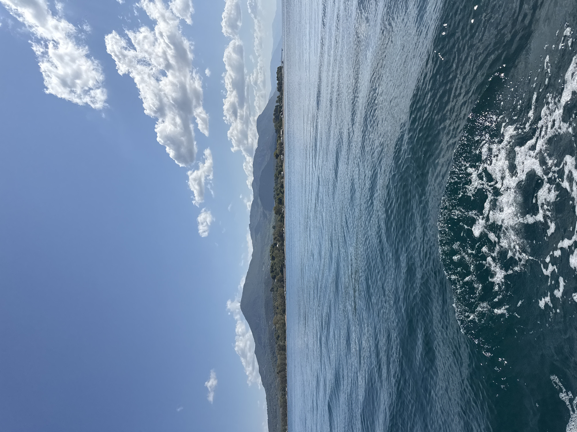 Boat cuts through calm Greek waters toward a wooded island