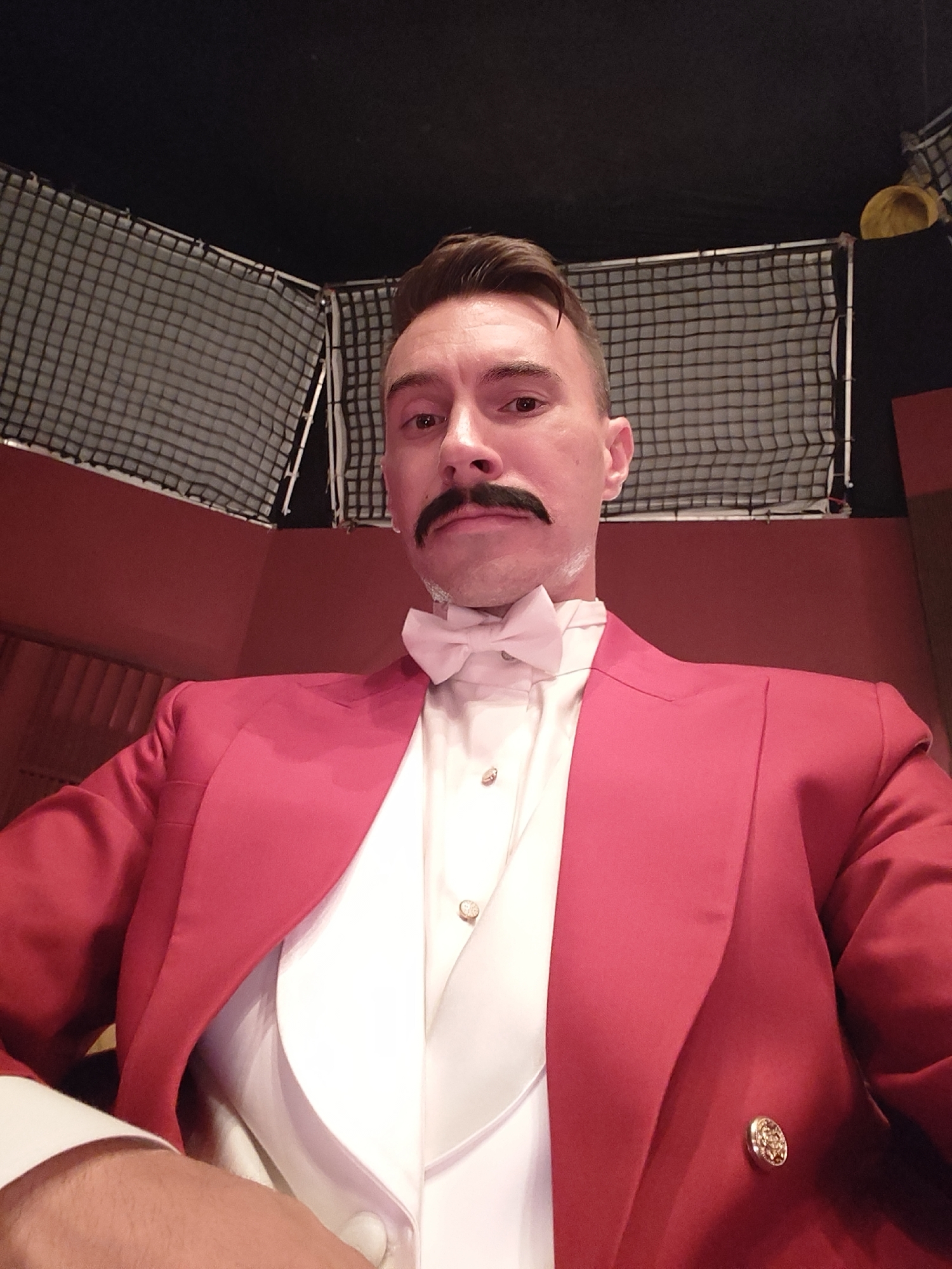 Man in formal red attire spotted under ornate chandelier