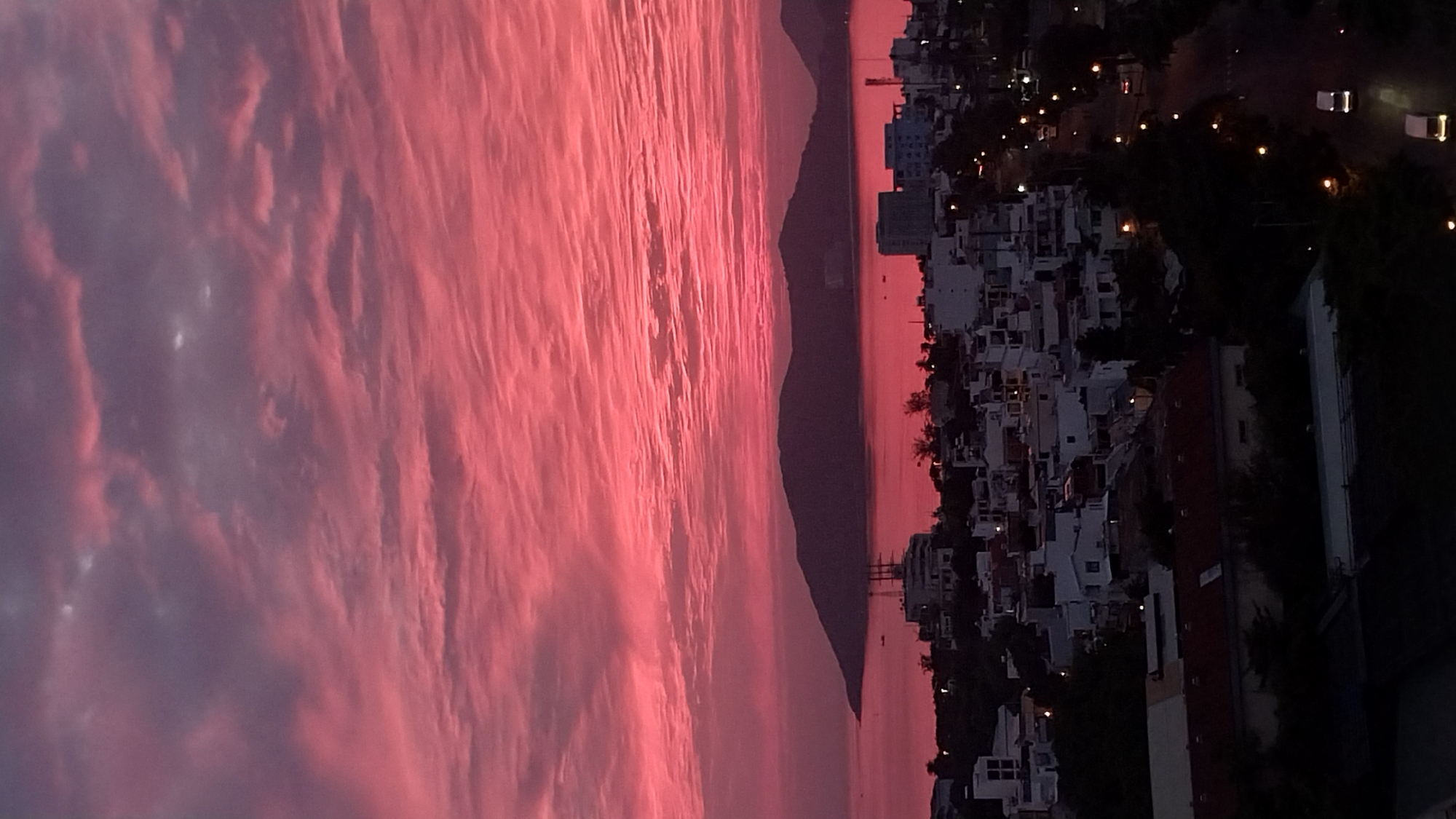 Fiery pink and red sunset lights up a coastal city skyline