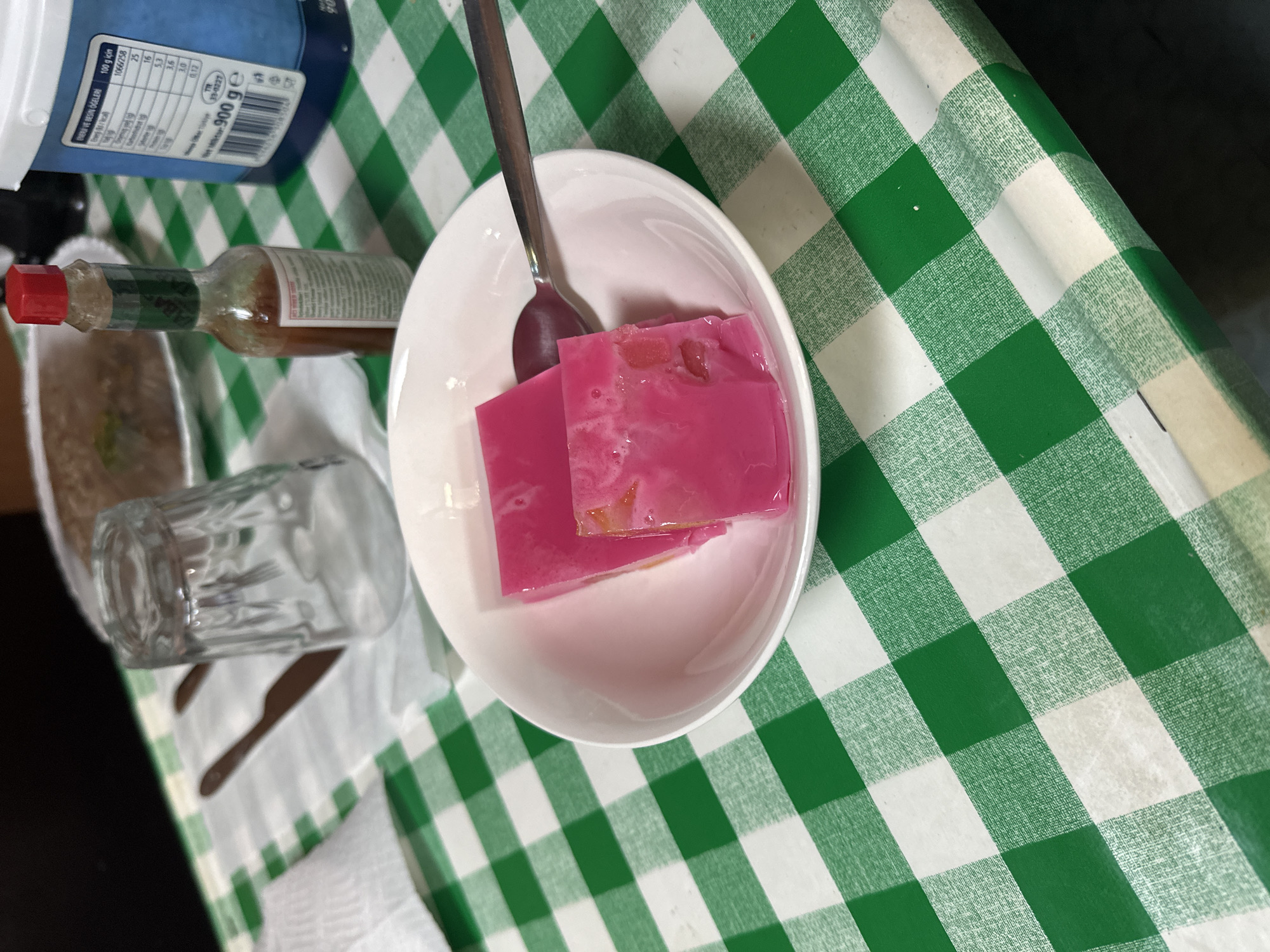 Pink gelatin dessert served in white bowl on checkered surface