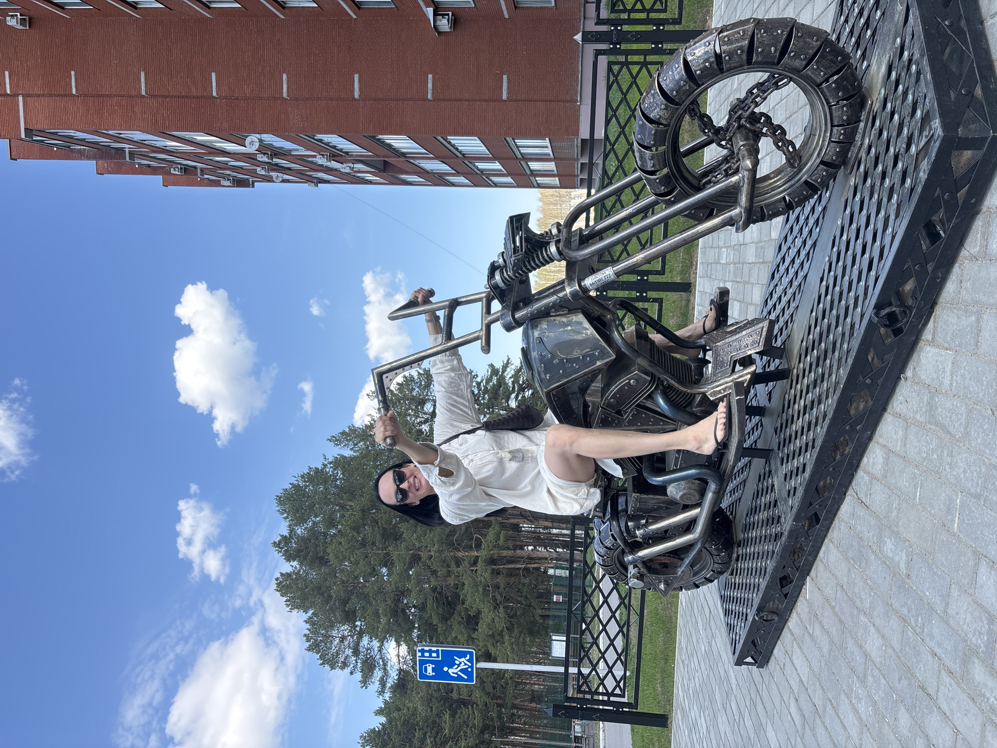 Woman poses with thumbs-up on motorcycle sculpture in Chaikovsky
