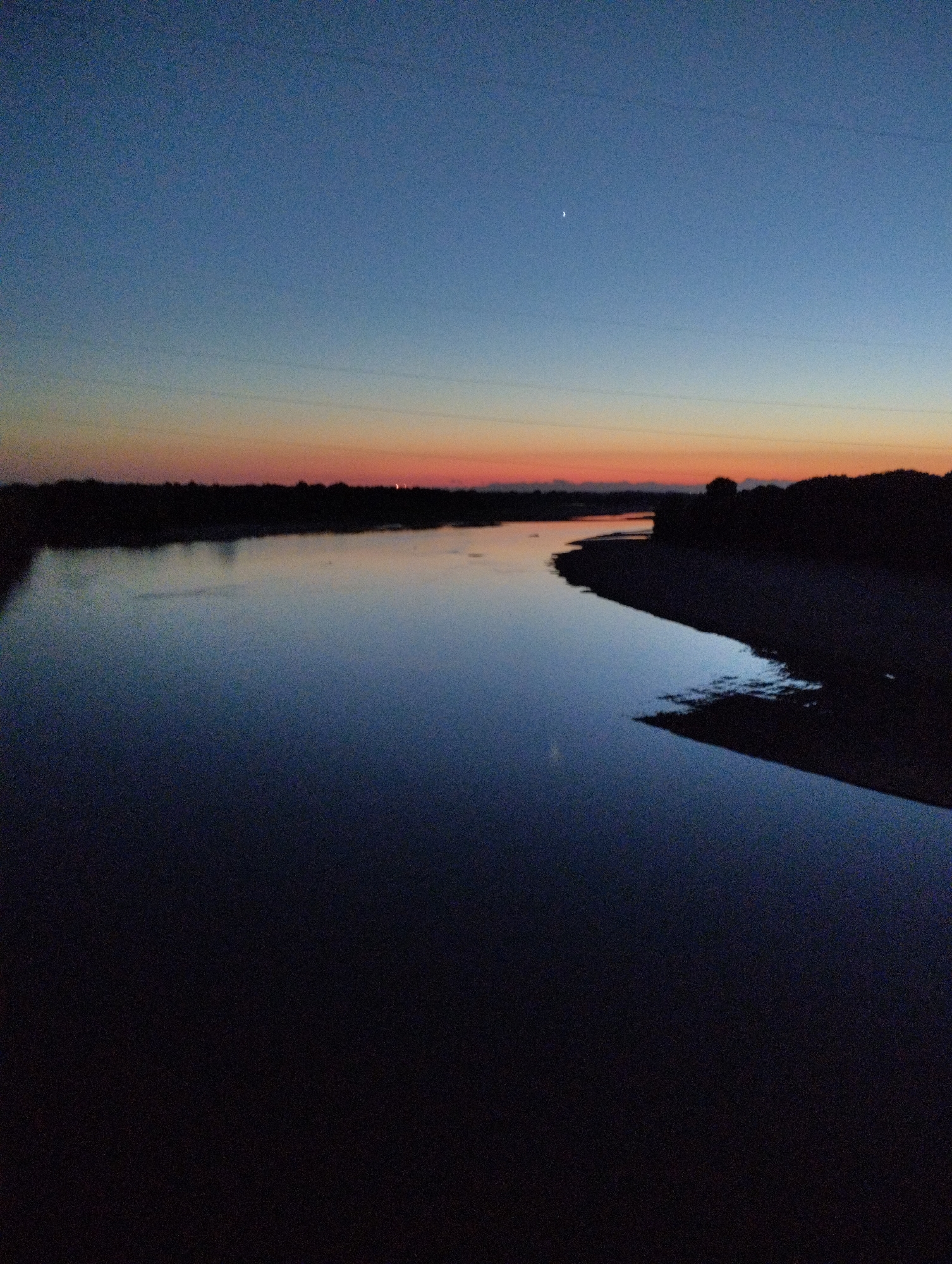 Crane lifts debris from structure near river at dusk