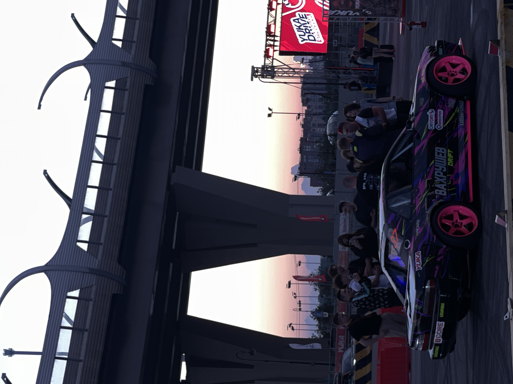 Urban drift meet draws modified cars under a highway overpass at dusk