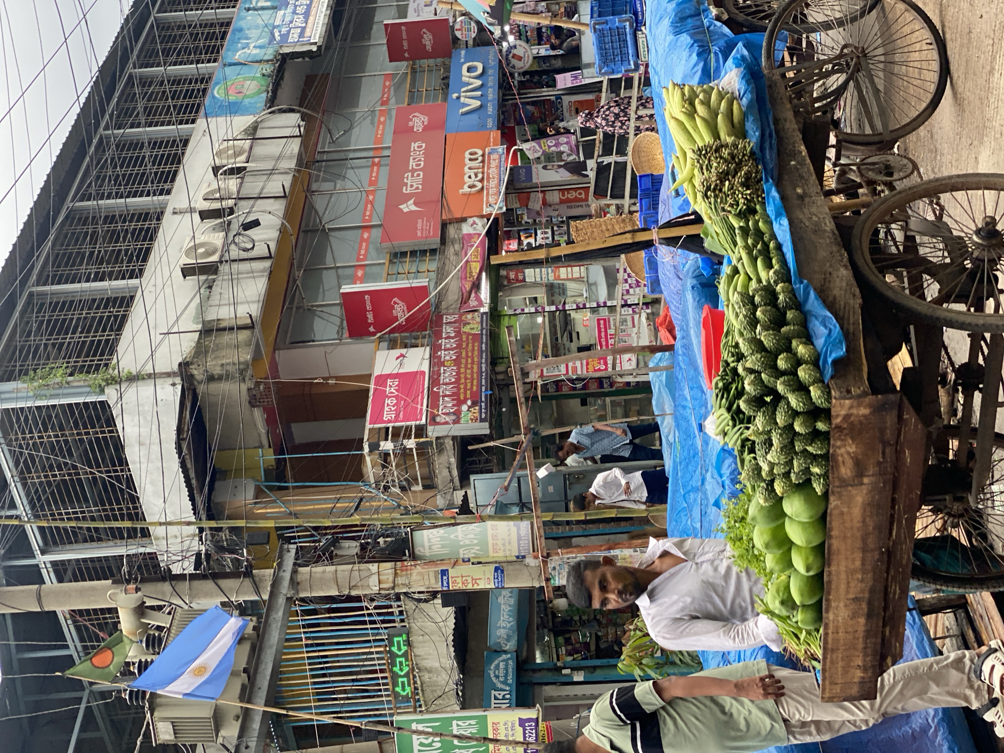 Dhaka street life: produce carts and mixed traffic on a cloudy morning