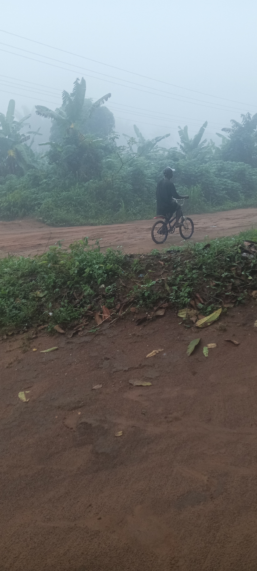 Cyclist navigates foggy dirt road in Amauzu, Nigeria