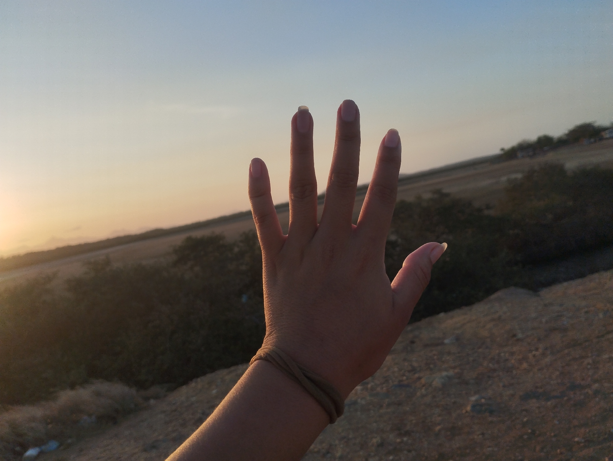 Hand gesture photographed against sunset sky in Venezuelan coastal town