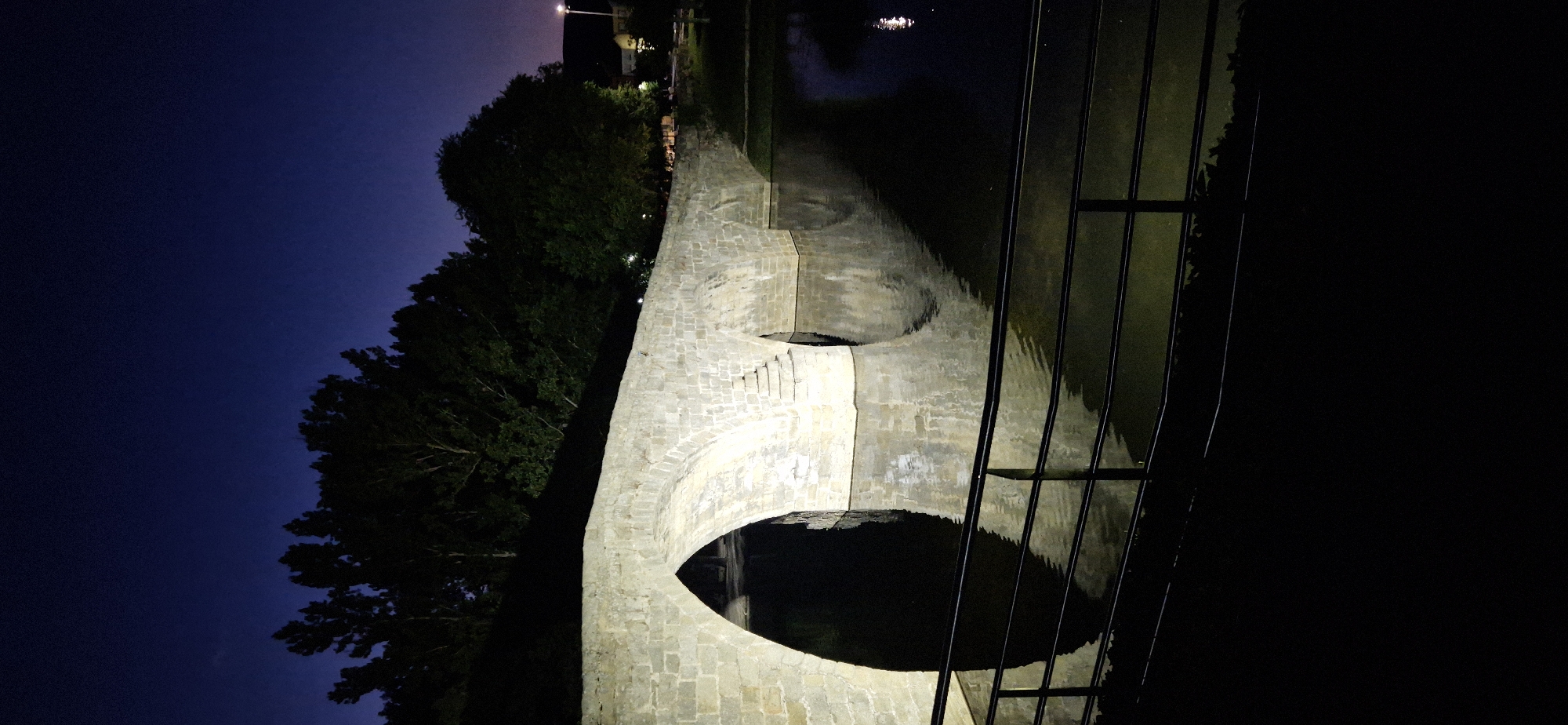 Navaluenga at night: stone bridges, lit pathways, and neon signage