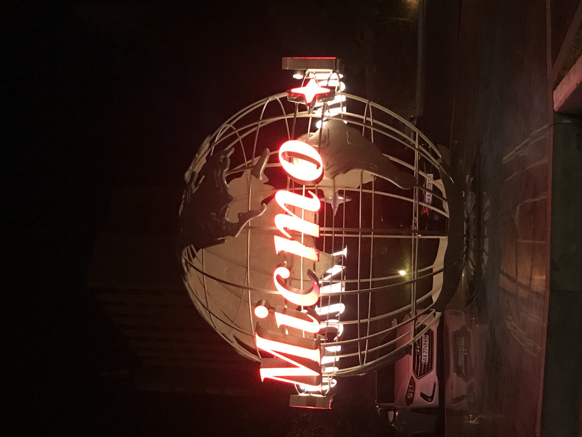 Illuminated wireframe globe sculpture with red neon signage at night