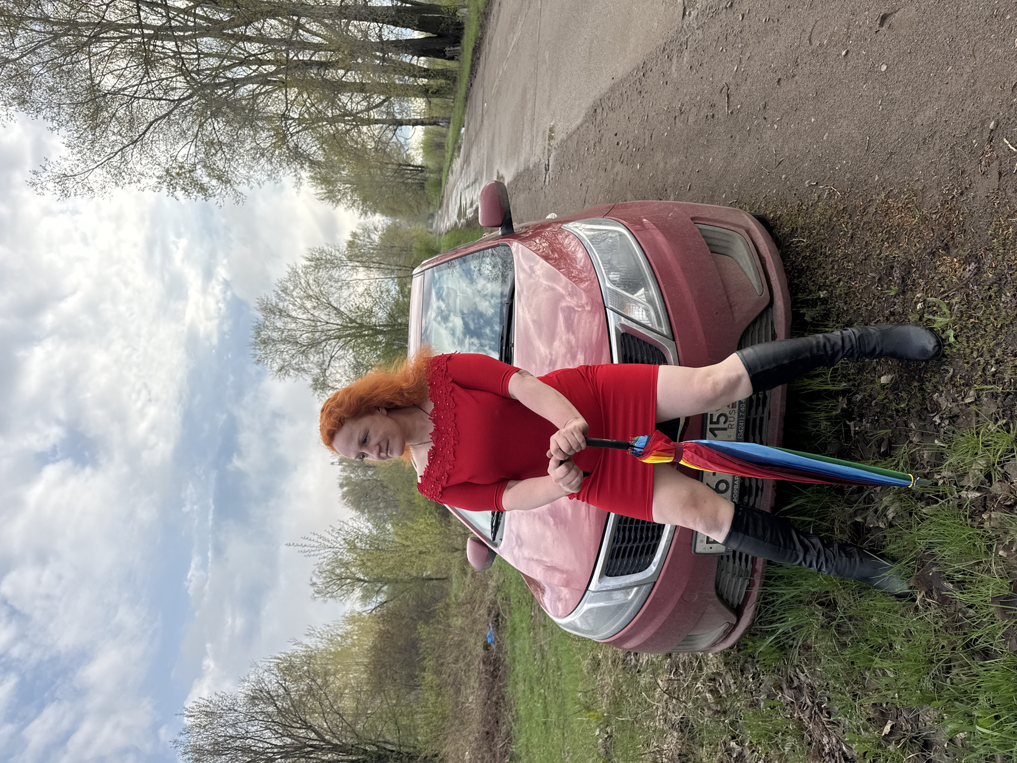 Woman in red poses with rainbow umbrella in rural Russia