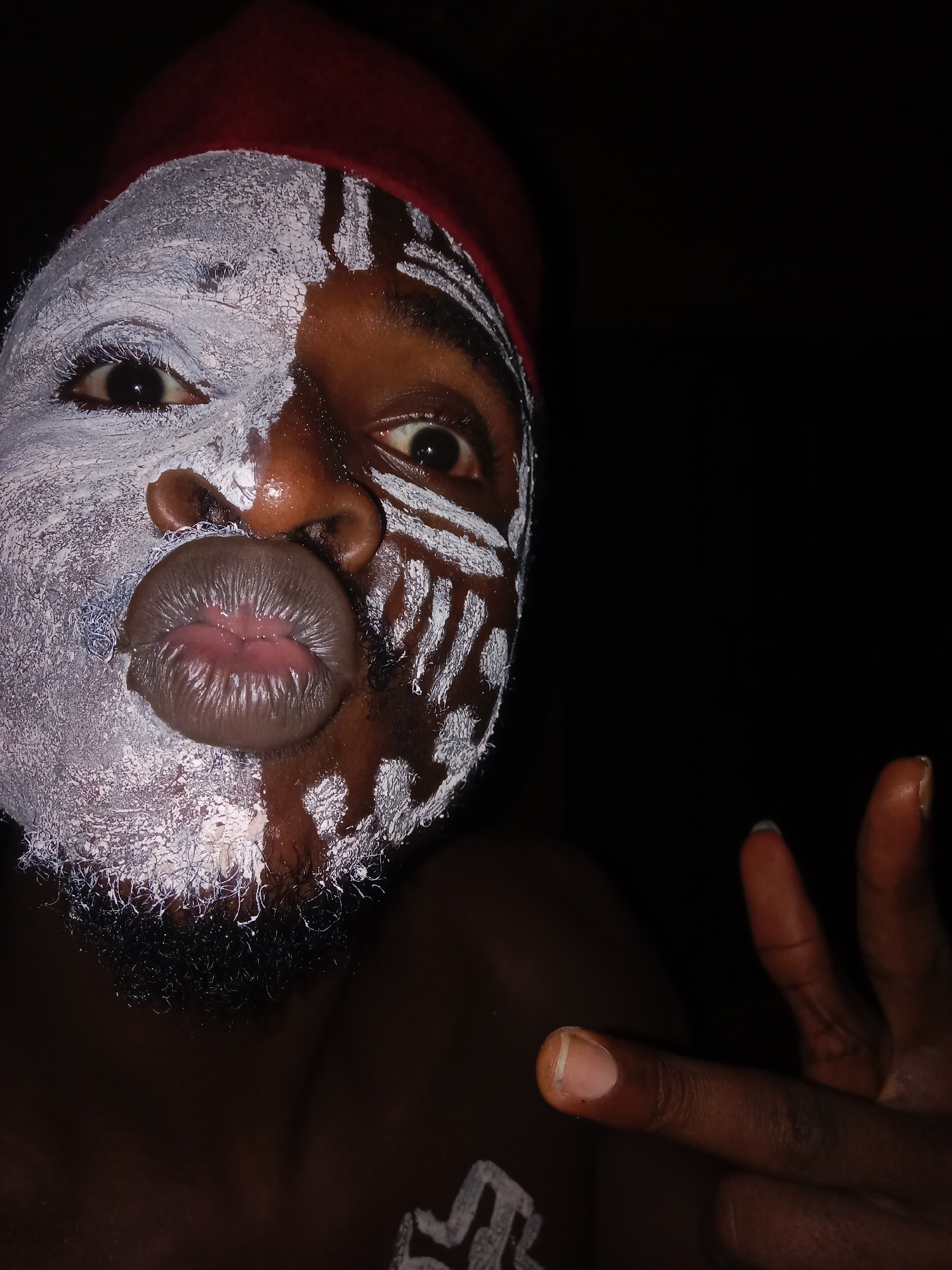 Person in red fez displays elaborate white tribal face paint