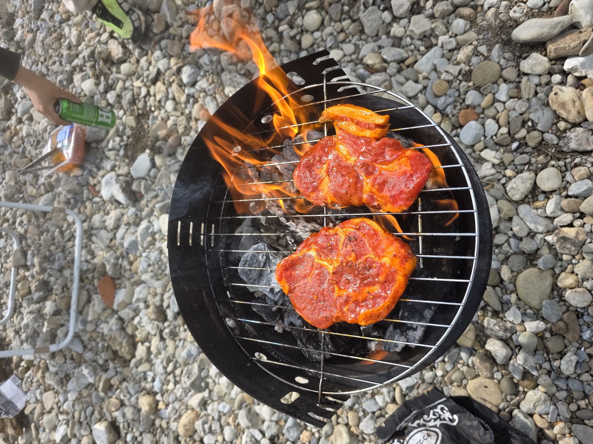 Riverside camping scene with fire pit and chairs observed