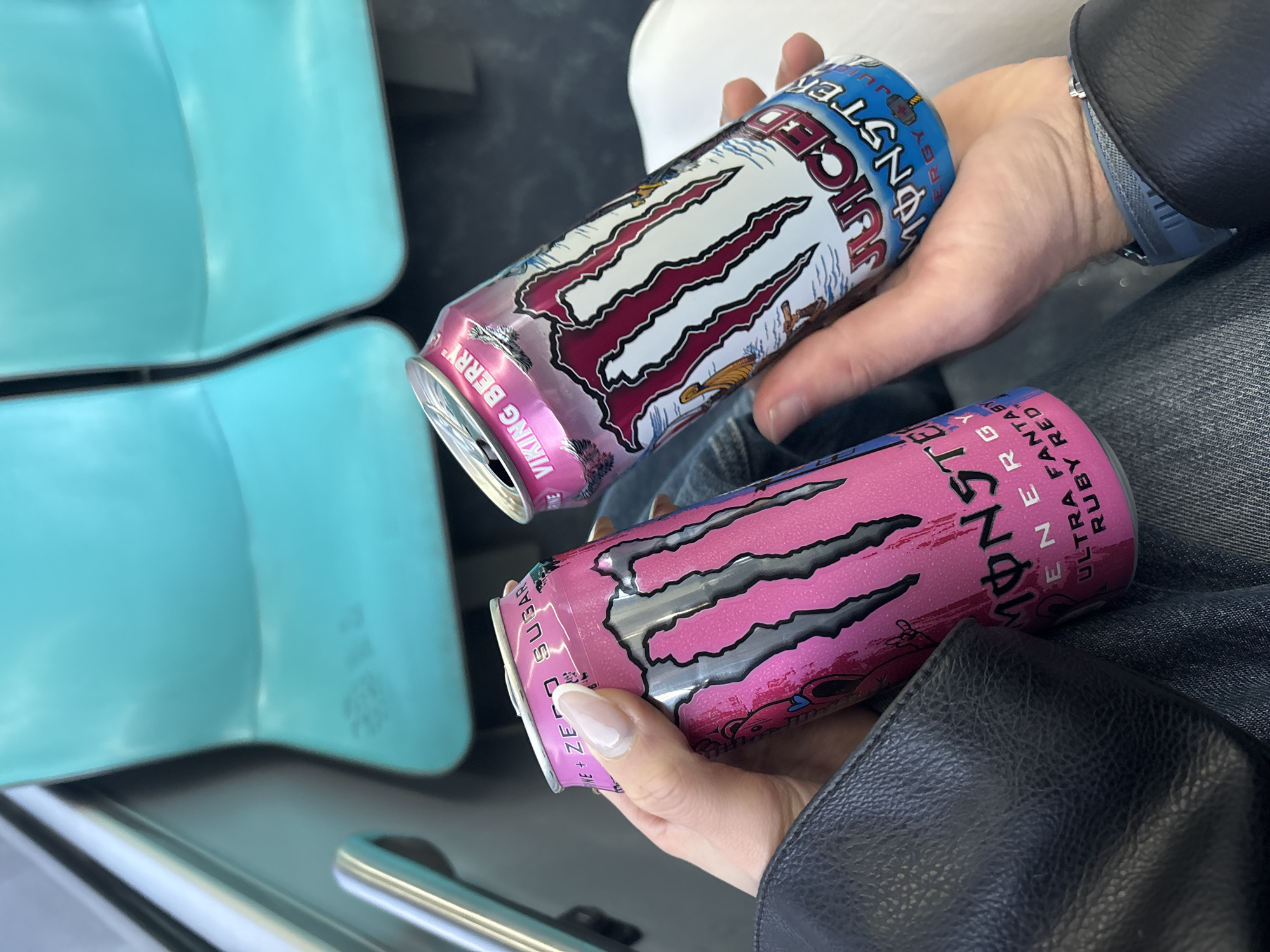 Person holds two Monster energy drinks in vehicle