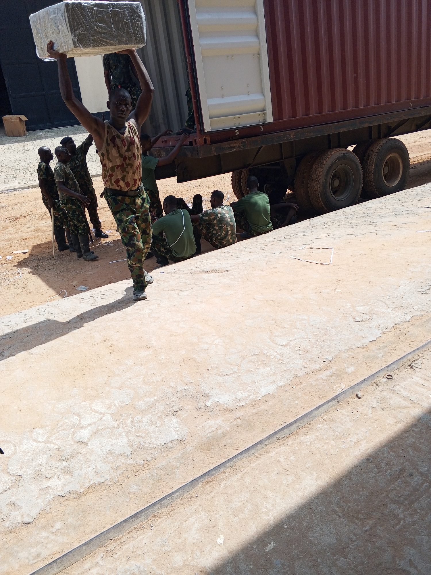 Military-dressed group gathers near truck, person carries wrapped package