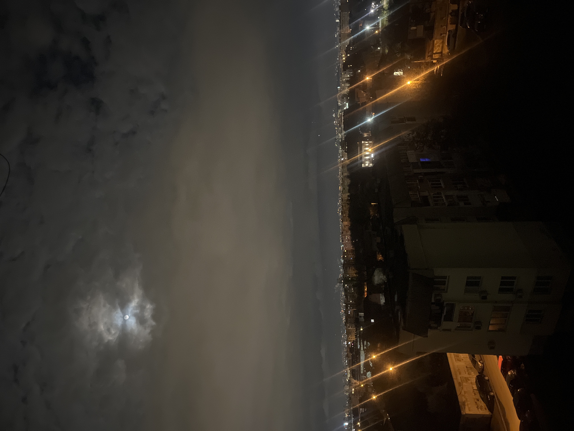 Moon breaks through clouds over Sofia's illuminated nighttime skyline