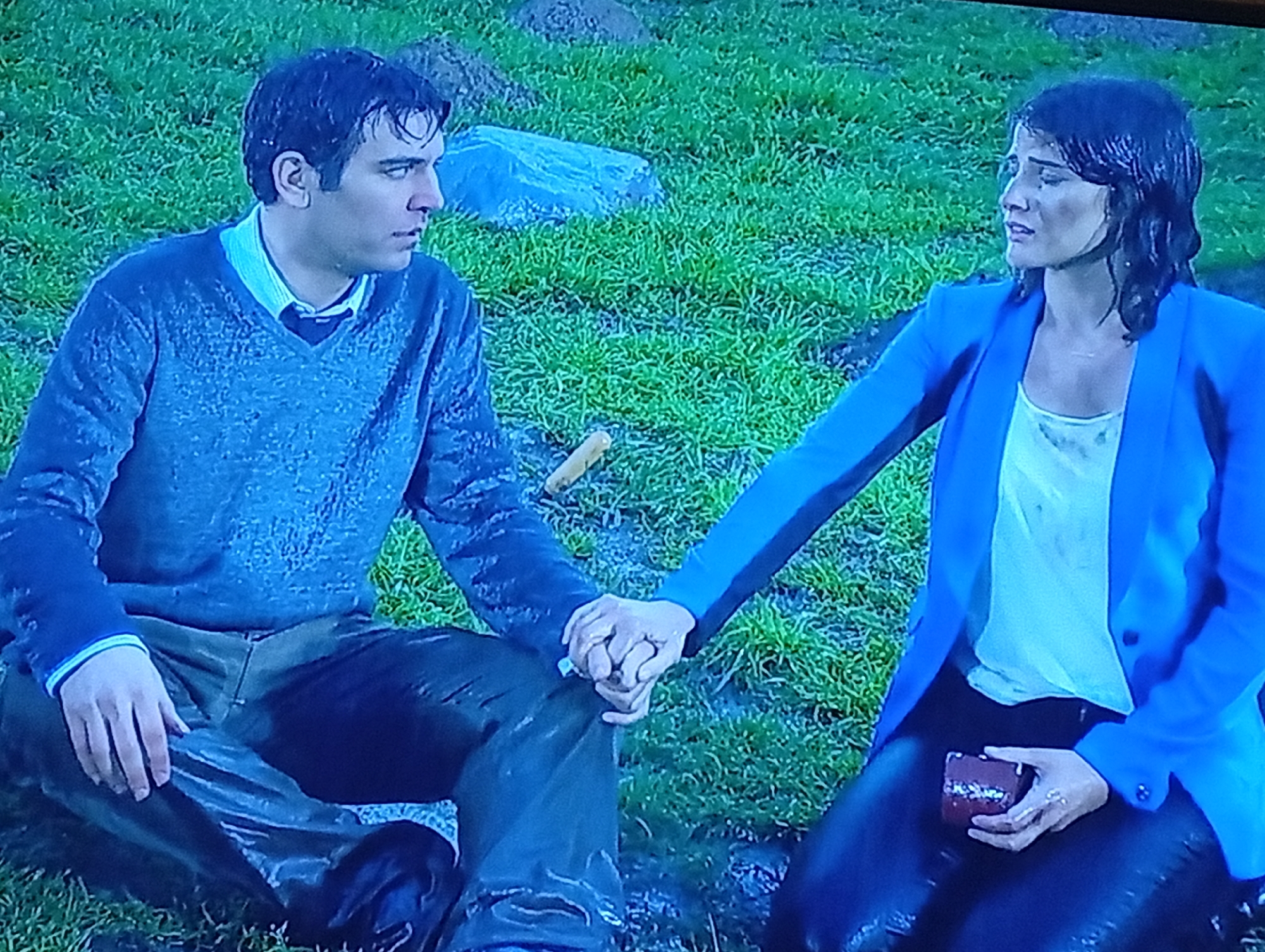 Couple sits in wet grass; coffee machine operated nearby